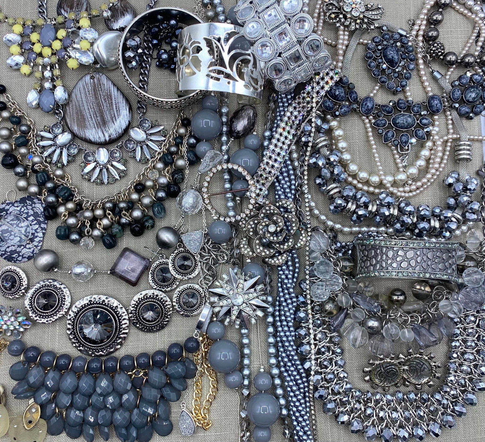 Monochromatic Costume Jewelry: An assortment of contemporary costume jewelry primarily featuring a monochromatic color palette of silver, gray, black, and clear tones. The collection includes necklaces such as a silver tone chain w