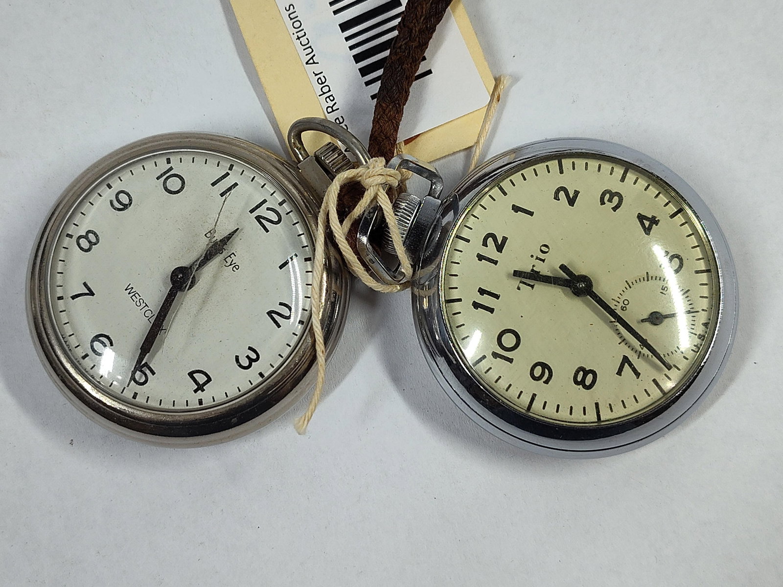 Pair Vtg Westclox & Trio Pocket Watches: This lot comprises two mid-20th-century American open-face pocket watches. The first is a Westclox Bulls Eye model, featuring a silver-tone base metal case and a white dial with black Arabic numerals