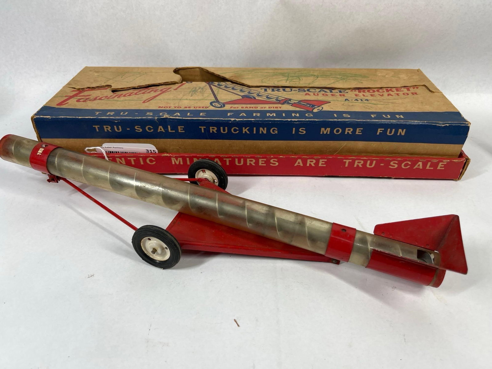 Tru-Scale Rocket Auger Elevator w/ Box: This vintage 1:16 scale farm toy is a Tru-Scale Rocket Auger Elevator, model number A-414. The piece is constructed with a red-painted die-cast metal frame, base, and intake hopper. A clear plastic