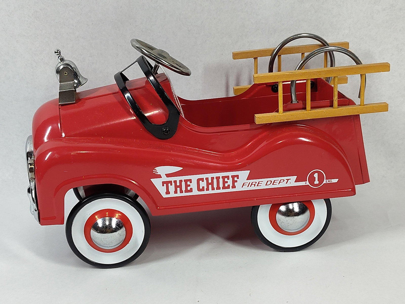 Pressed Steel Fire Engine Pedal Car: 10 inches. This item is a contemporary decorative scale model of a fire engine truck, designed to replicate the appearance of a mid-century vintage pedal car. The body is constructed from bright red