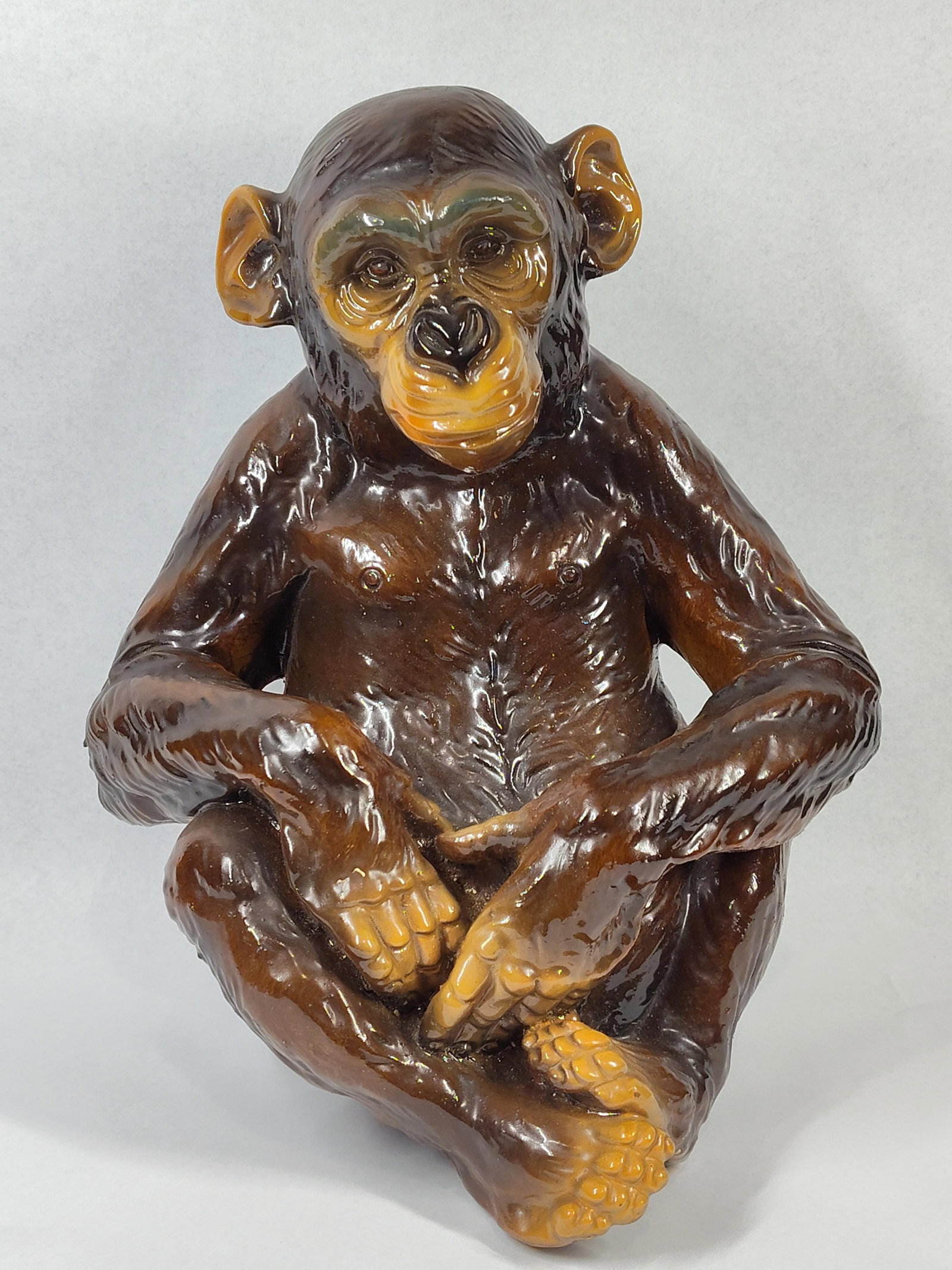 Glazed Carved Wood Chimpanzee Figurine: 13x11x8 This figurine depicts a seated chimpanzee in a naturalistic pose with its hands resting in its lap. The piece is constructed from a carved wood core, visible on the unglazed portion of the