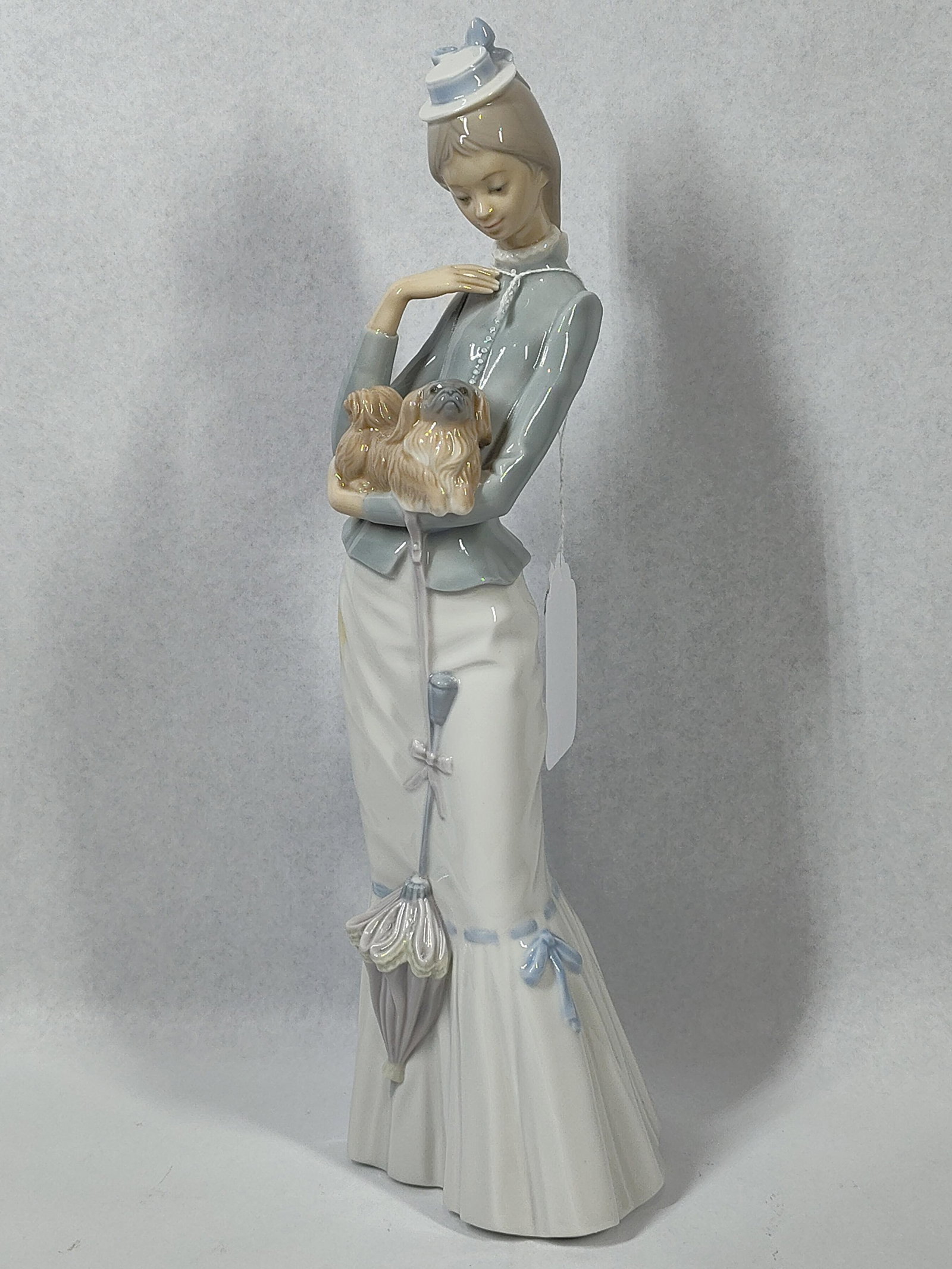 Lladro Style Porc. Figurine w/ Parasol: 15 in. This glazed porcelain figurine, attributed to Lladro, corresponds to model number 4893, titled A Walk with the Dog, and was sculpted by Salvador Furio. The piece depicts a slender young woman