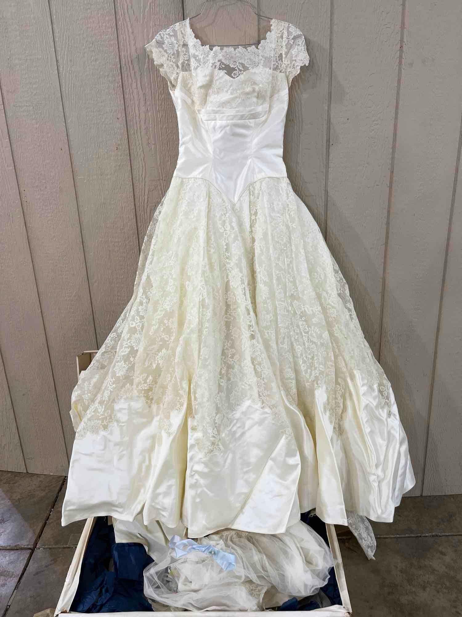1950s Satin & Floral Lace Wedding Gown: A mid-century bridal gown constructed from cream-colored satin and floral lace. The bodice features a scalloped lace overlay at the neckline and short cap sleeves, situated above horizontal ruched