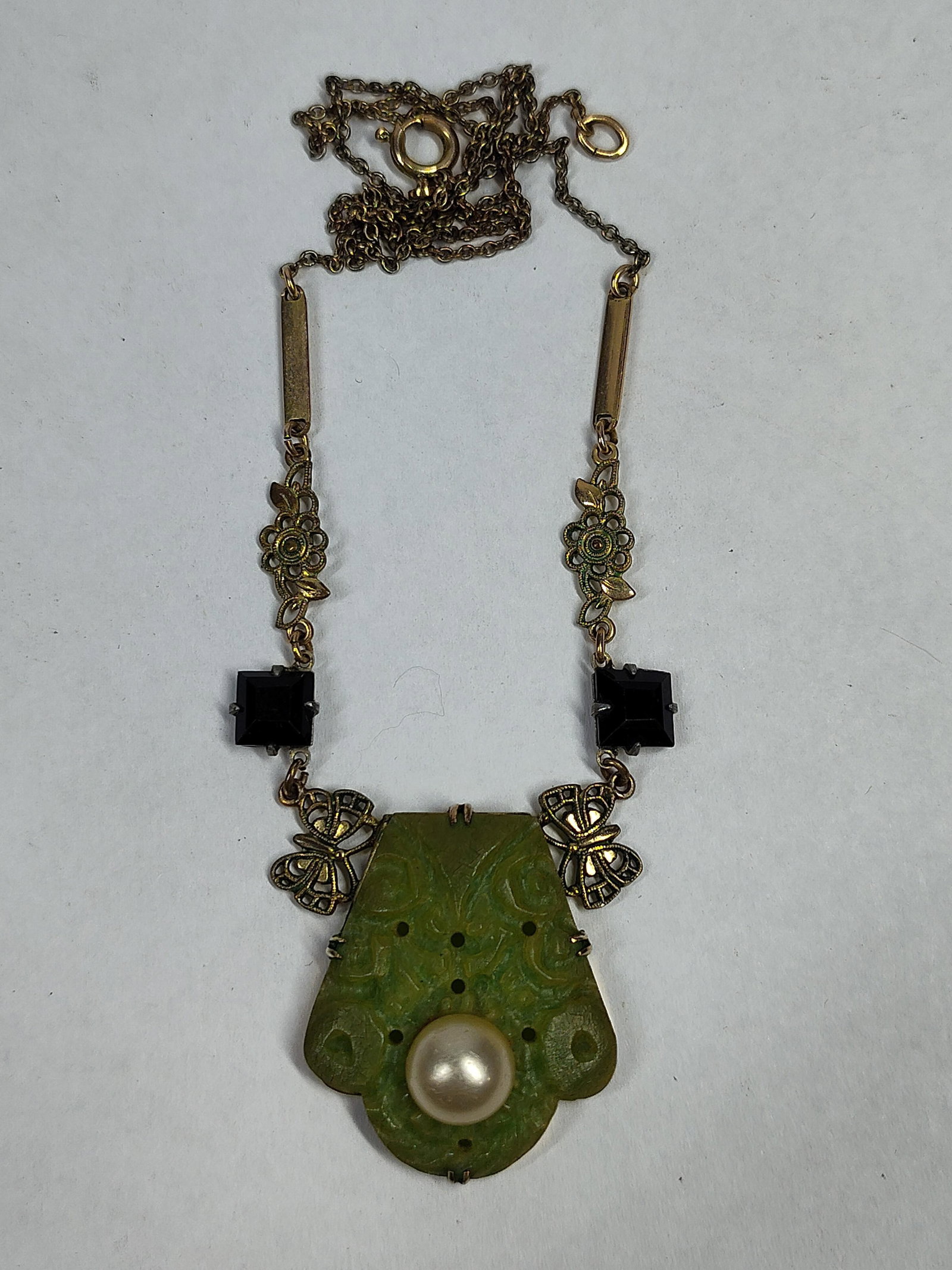 Czechoslovakian Art Deco Glass Necklace: An Art Deco style pendant necklace featuring a central shield-shaped pendant of carved green molded glass made to resemble jade. The pendant is inset with a large white button-shaped simulated pearl. 