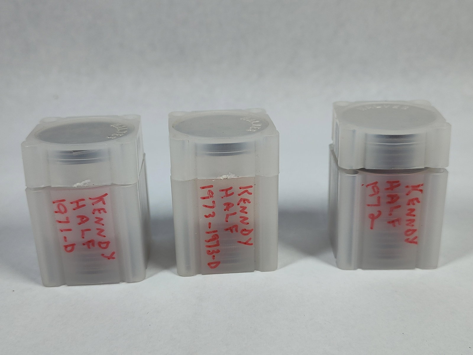 US Kennedy Half Dollars in Square Tubes: A collection of US Kennedy half dollars (KM# 202b) housed in three translucent square plastic coin storage tubes. The coins are struck in a copper-nickel clad composition. Based on the handwritten lab