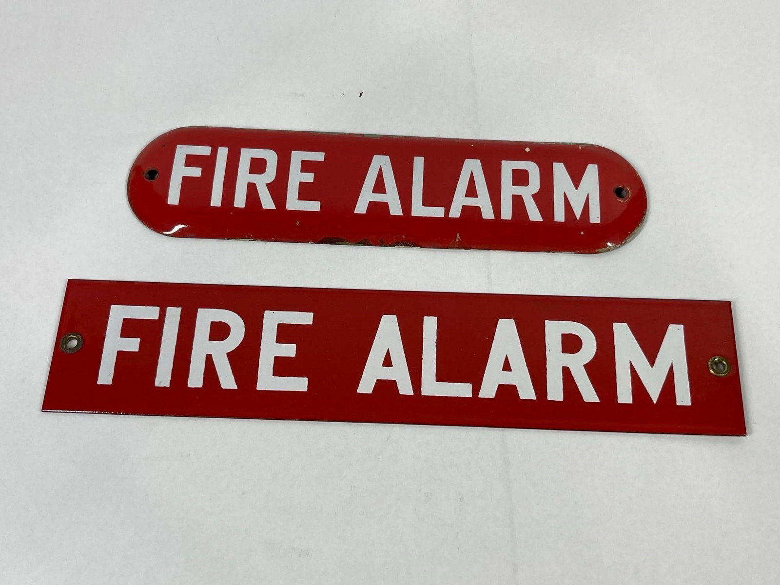 Two Vintage Red Fire Alarm Signs: 12x2.5 and 10x2.5 This lot consists of two vintage fire safety identification signs. The first is an oval sign made of porcelain enamel on metal with a convex profile. It features a red background