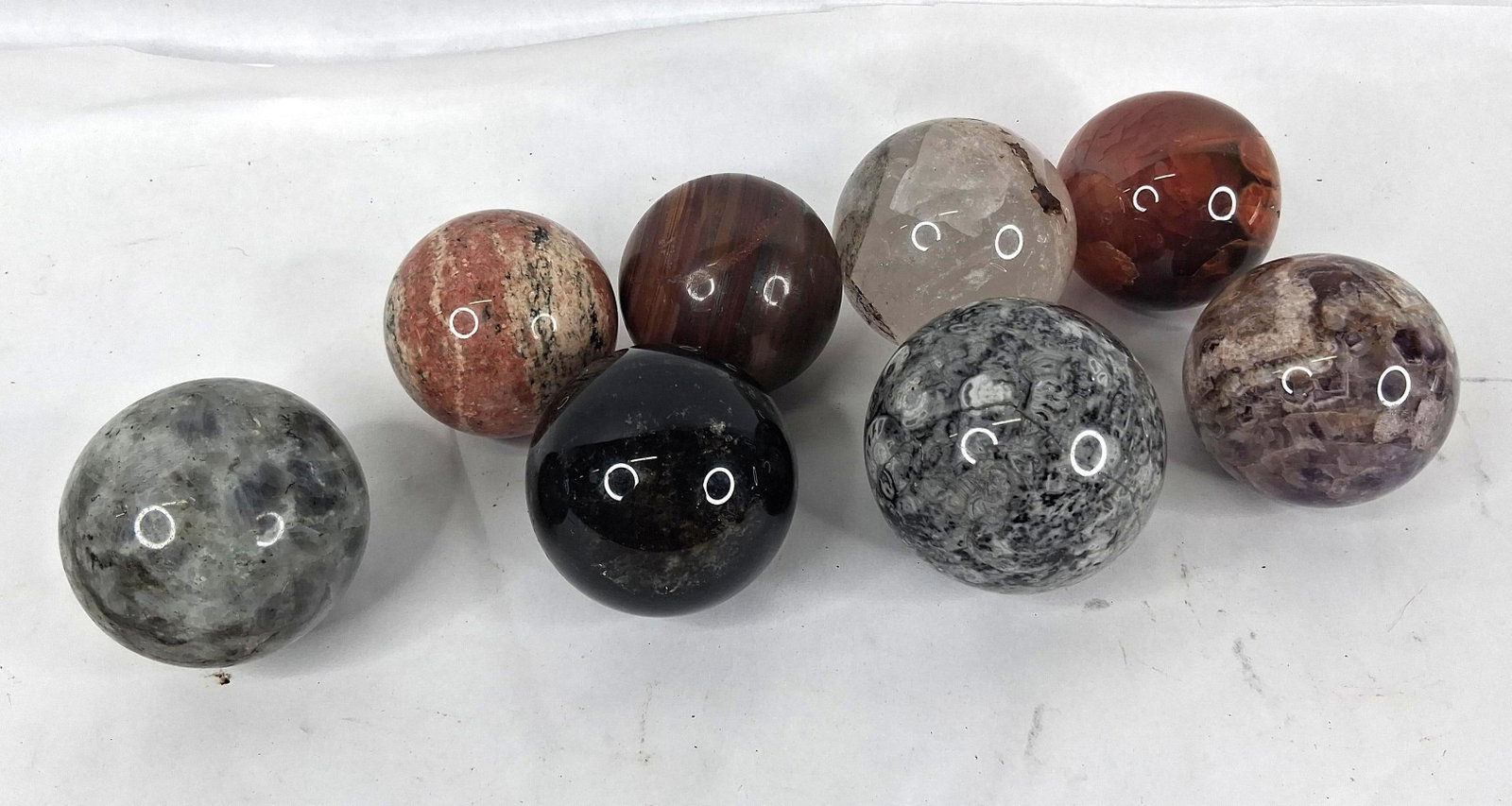 Set 8 Polished Mineral & Fossil Spheres: This lot features eight polished stone spheres showcasing a variety of natural geological materials. The collection includes one labradorite sphere exhibiting labradorescence with blue and green flash