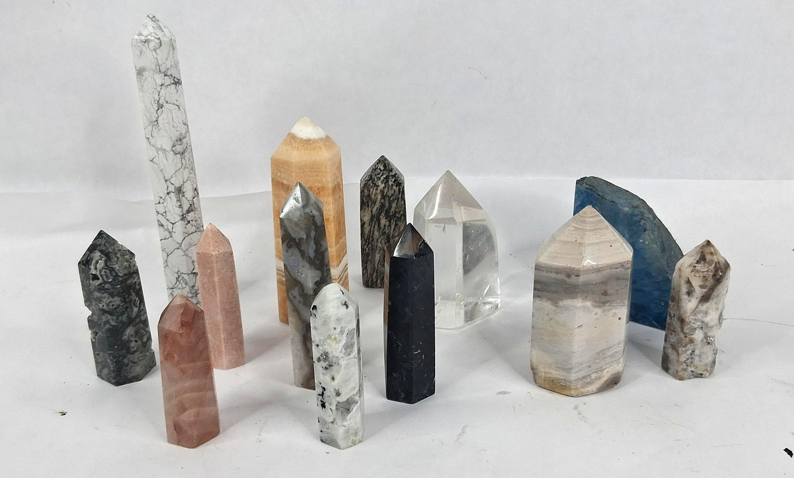 13 Polished Mineral Towers & Specimens: A collection of 13 decorative mineral specimens comprising 12 polished towers or points of varying heights and one large semi-circular slab with a polished face. The towers exhibit a range of mineral