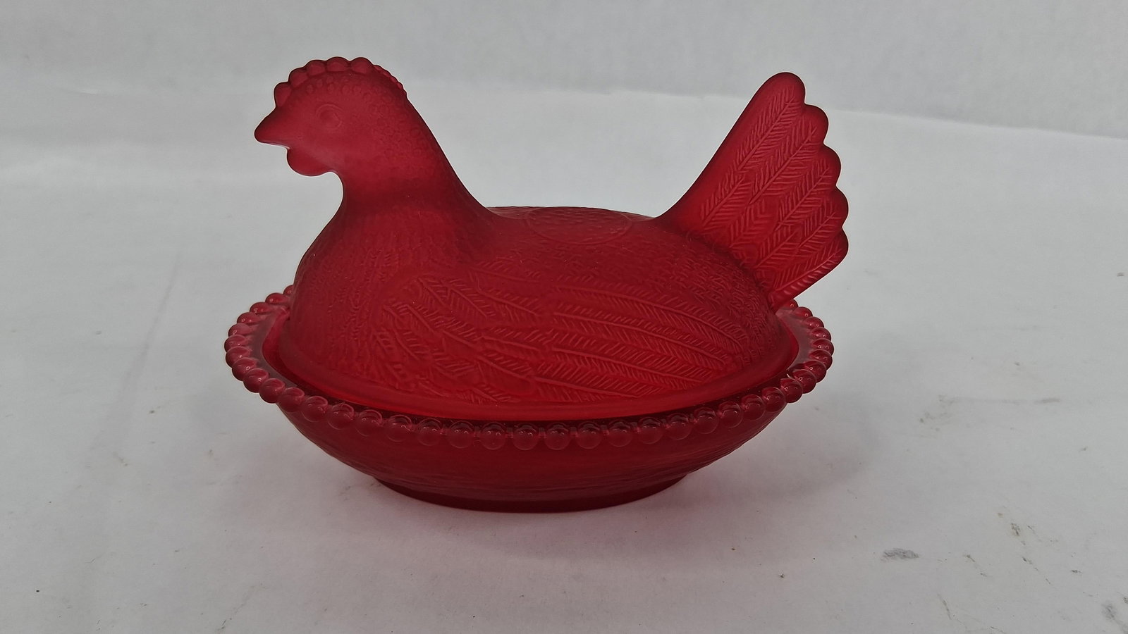Red Satin Glass Hen on Nest Beaded Dish: 4.5 in long This two-piece molded glass covered dish is designed in the traditional hen on nest form. The item is crafted from vibrant ruby red glass that has been treated with a uniform frosted