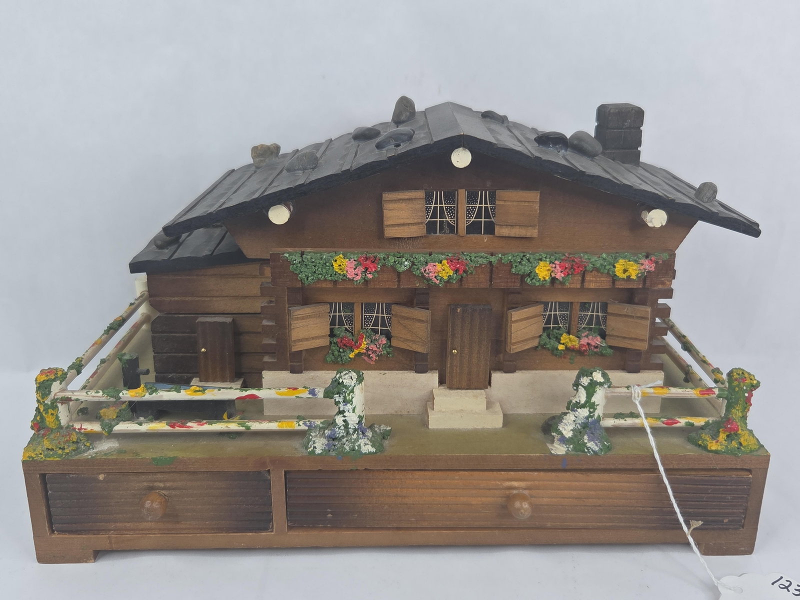 Swiss Chalet Music Box w/ Ballerina: A vintage musical jewelry box designed in the style of a traditional Swiss alpine chalet. The structure is crafted from stained and painted wood, featuring a pitched shingled roof decorated with