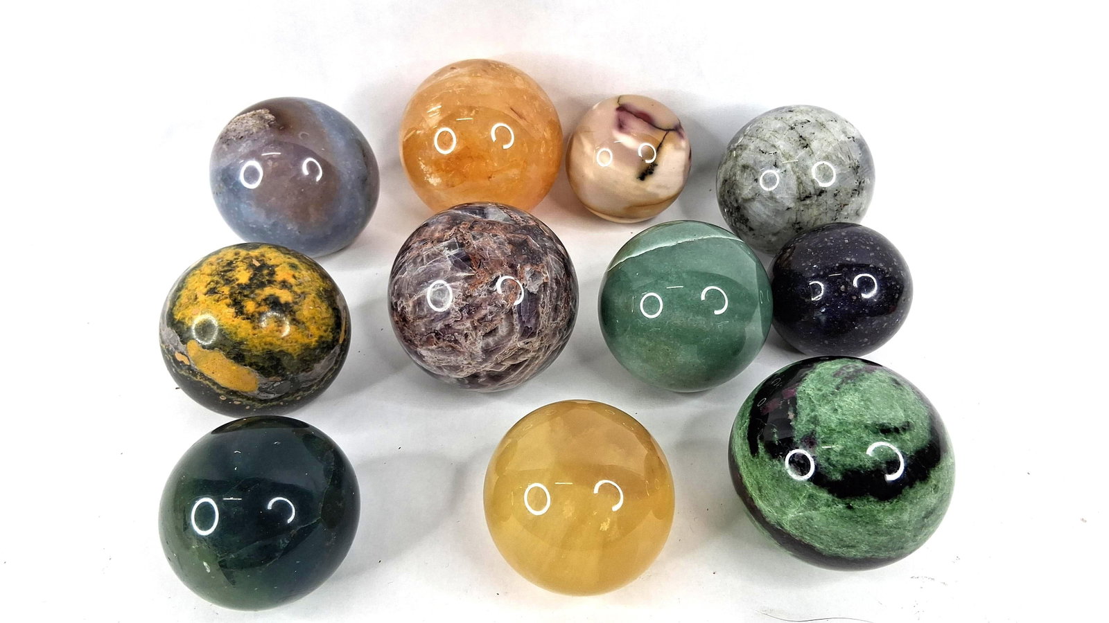 Polished Mineral & Gemstone Spheres: This collection consists of multiple polished mineral and gemstone spheres of varying sizes. Based on visual characteristics, the specimens include a green zoisite sphere with pink ruby and black