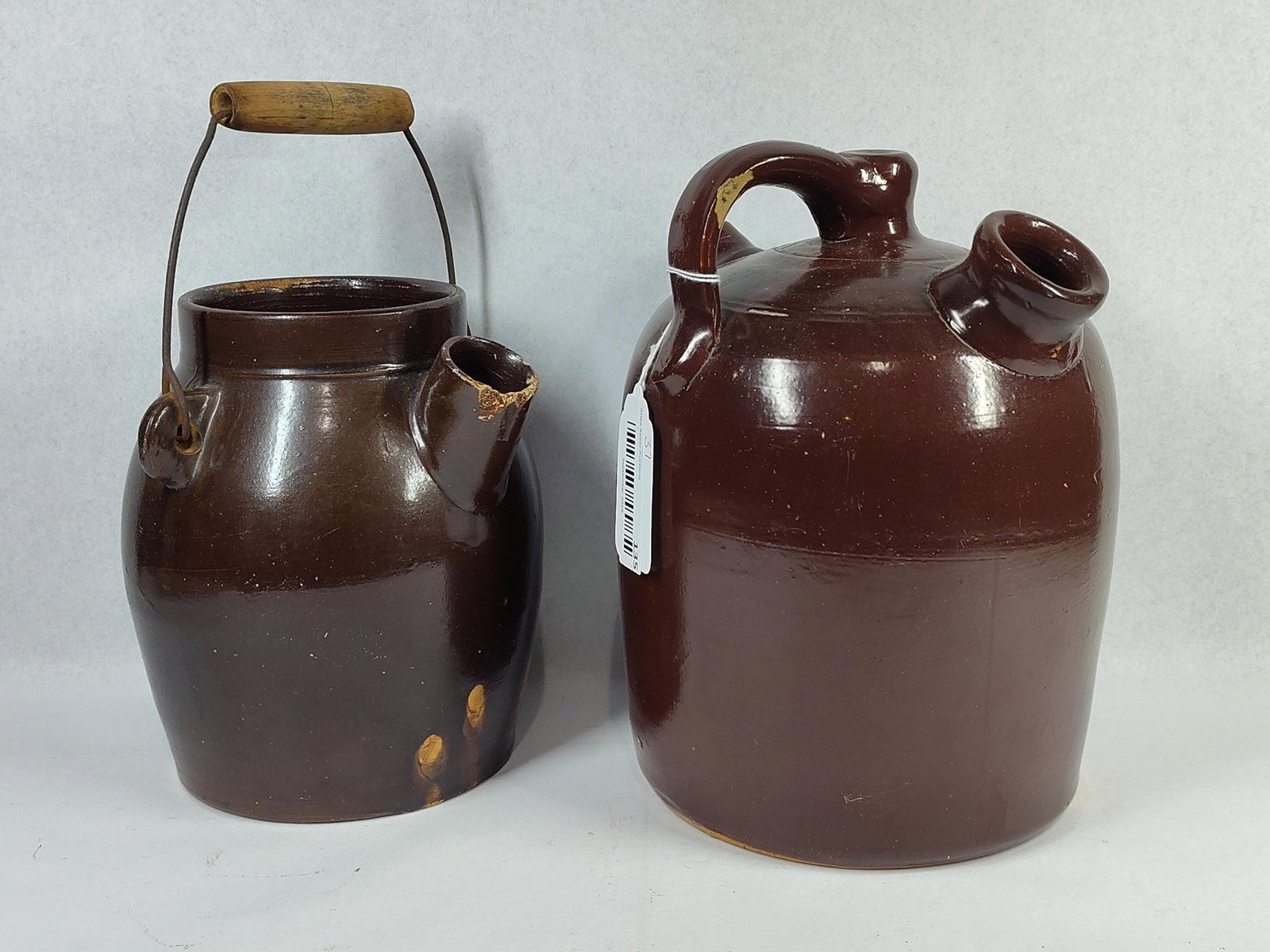 Pair American Albany-Slip Vessels: This lot contains two American stoneware vessels finished in a dark brown Albany-type slip glaze, dating from the late 19th to early 20th century. The first vessel is a batter jug featuring an ovoid