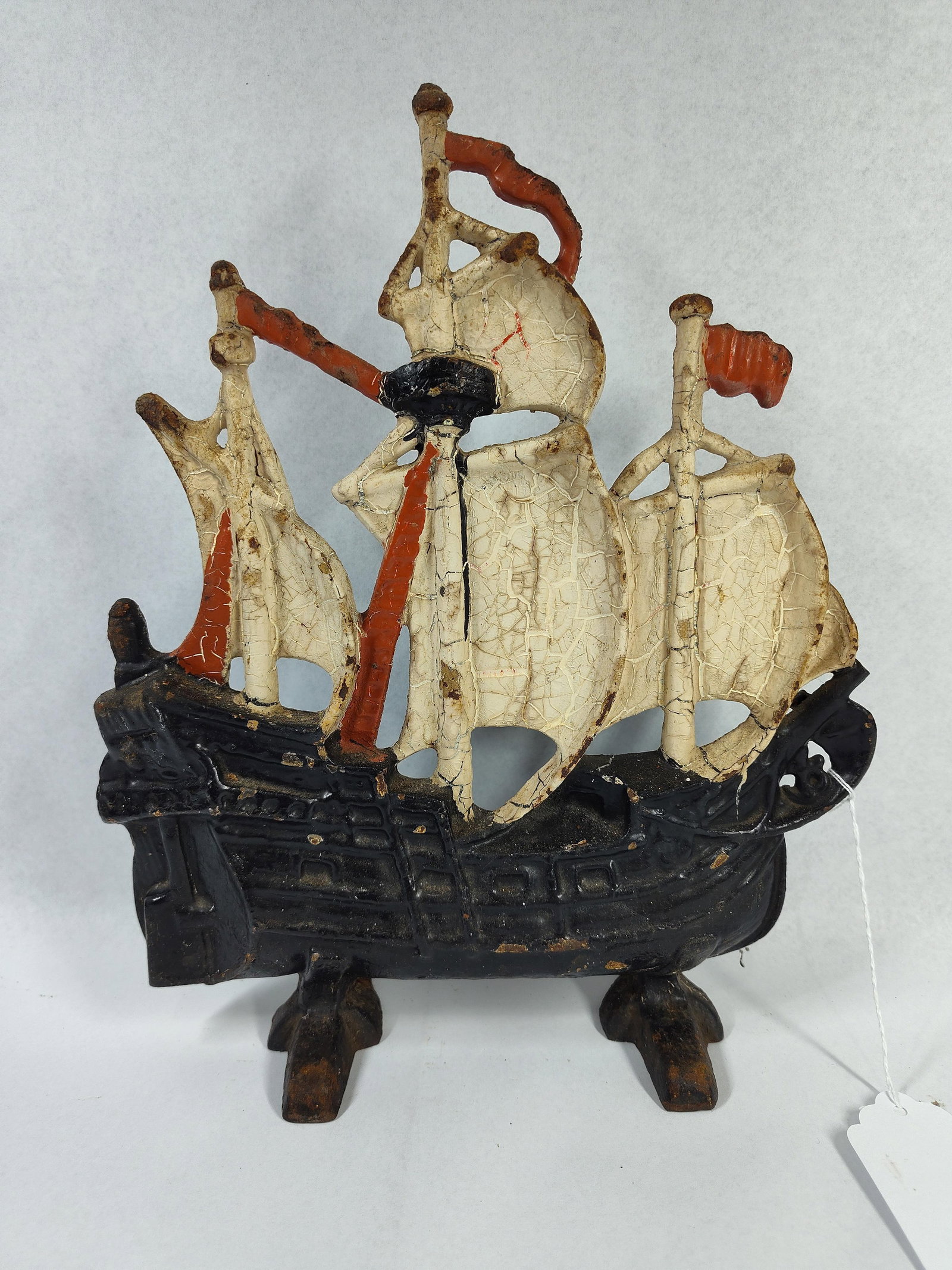 Polychrome Cast Iron Galleon Doorstop: A cast iron doorstop modeled as a three-masted galleon in full sail. The object is a single-sided relief casting featuring a flat reverse and is supported by two integrated feet at the base. The ship 