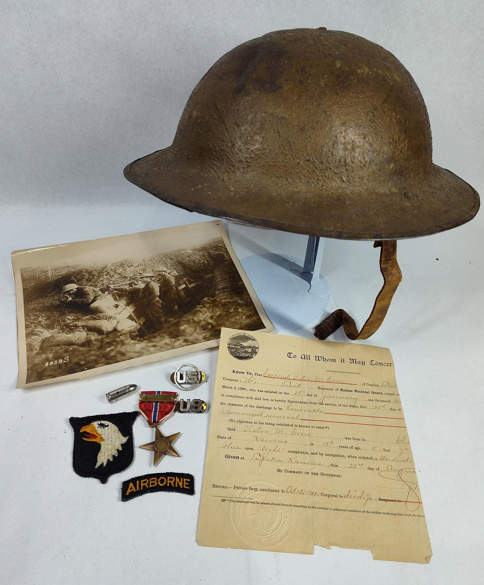 US Military WWI Helmet, Insignia & Doc: A group of United States military artifacts and ephemera spanning the early 20th century through World War II. The lot features a US M1917 steel helmet, often identified as the Brodie pattern, charact