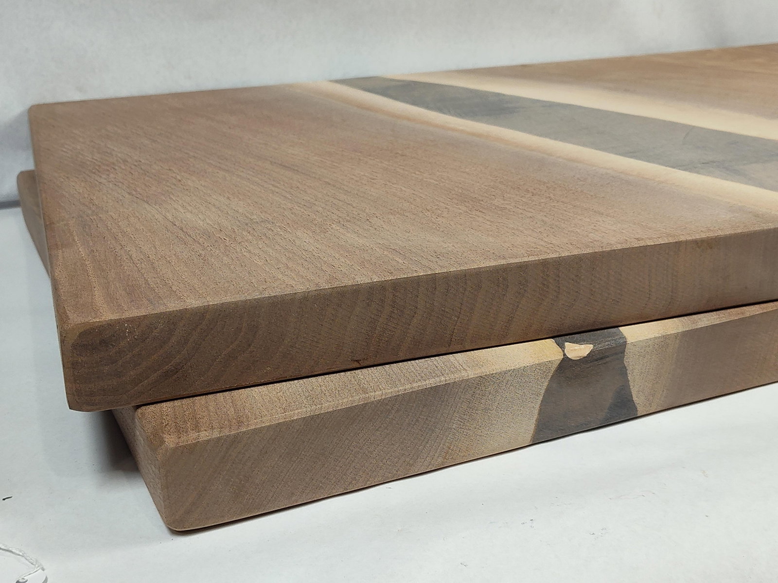 Pair Black Walnut & Resin River Boards: A pair of handcrafted river-style serving boards constructed from live-edge black walnut and dark gray epoxy resin. Each board consists of two walnut slabs joined by a central resin pour. The wood fea