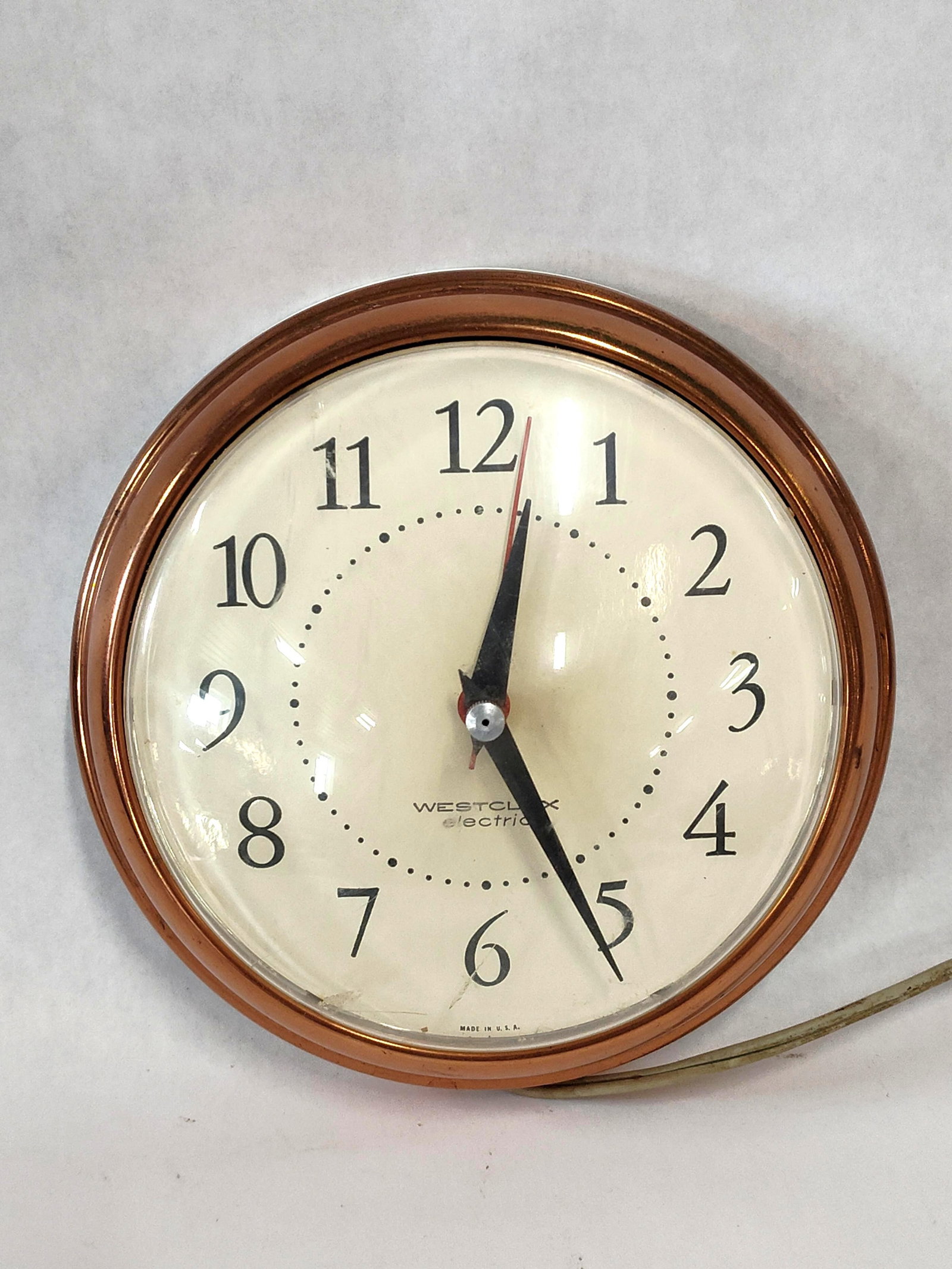 Westclox Spice Copper-Toned Wall Clock: This Westclox Spice model S13-G electric wall clock features a Mid-Century Modern aesthetic. The timepiece is constructed with a copper-toned metal bezel and a white rear housing. The off-white dial