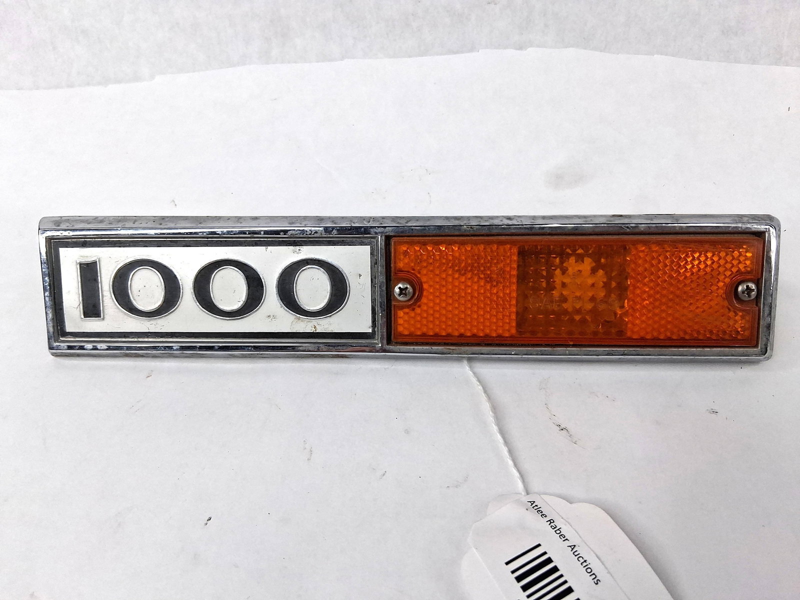 Int. Harvester 1000 Emblem & Side Light: This is a single genuine OEM automotive exterior trim assembly designed for the front fender of a vehicle. The unit combines a model designation badge with an integrated side marker light. The bezel a
