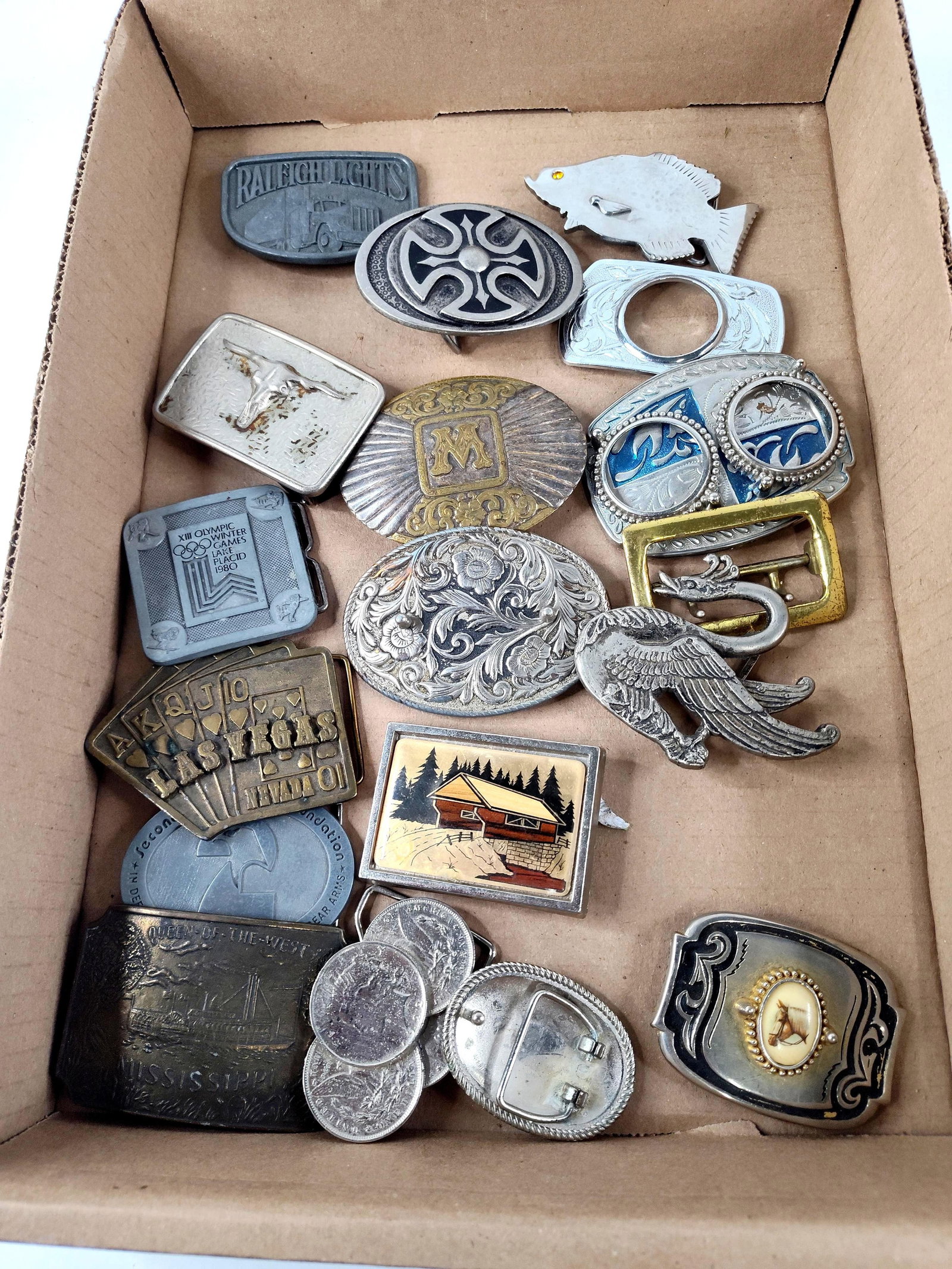 18 Vtg Western & Americana Belt Buckles: A collection of approximately 18 assorted and collectible belt buckles featuring various themes such as trucking, regional landmarks, and Western motifs. The lot includes a rectangular silver-tone