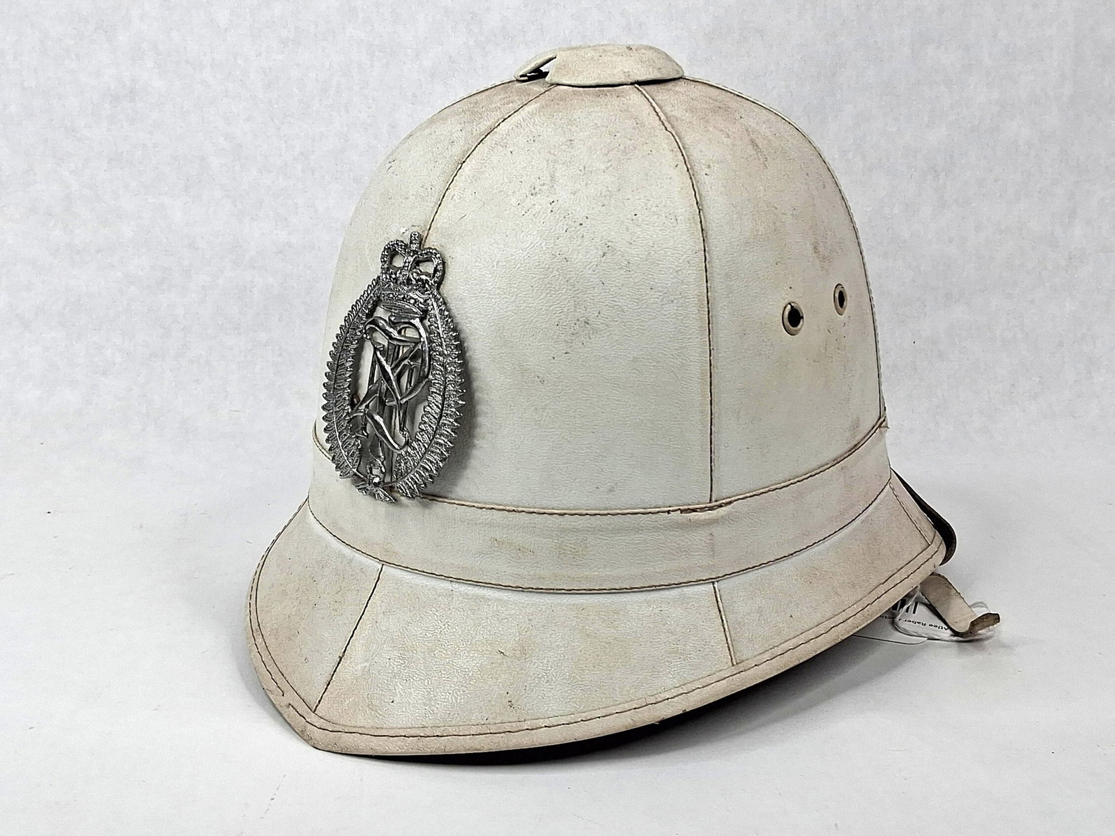 Mountcastle RPNGC Wolseley Pith Helmet: This white Wolseley pattern sun helmet is attributed to the Royal Papua New Guinea Constabulary (RPNGC). The helmet is constructed of multiple panels with a matching puggaree band. Centrally mounted o