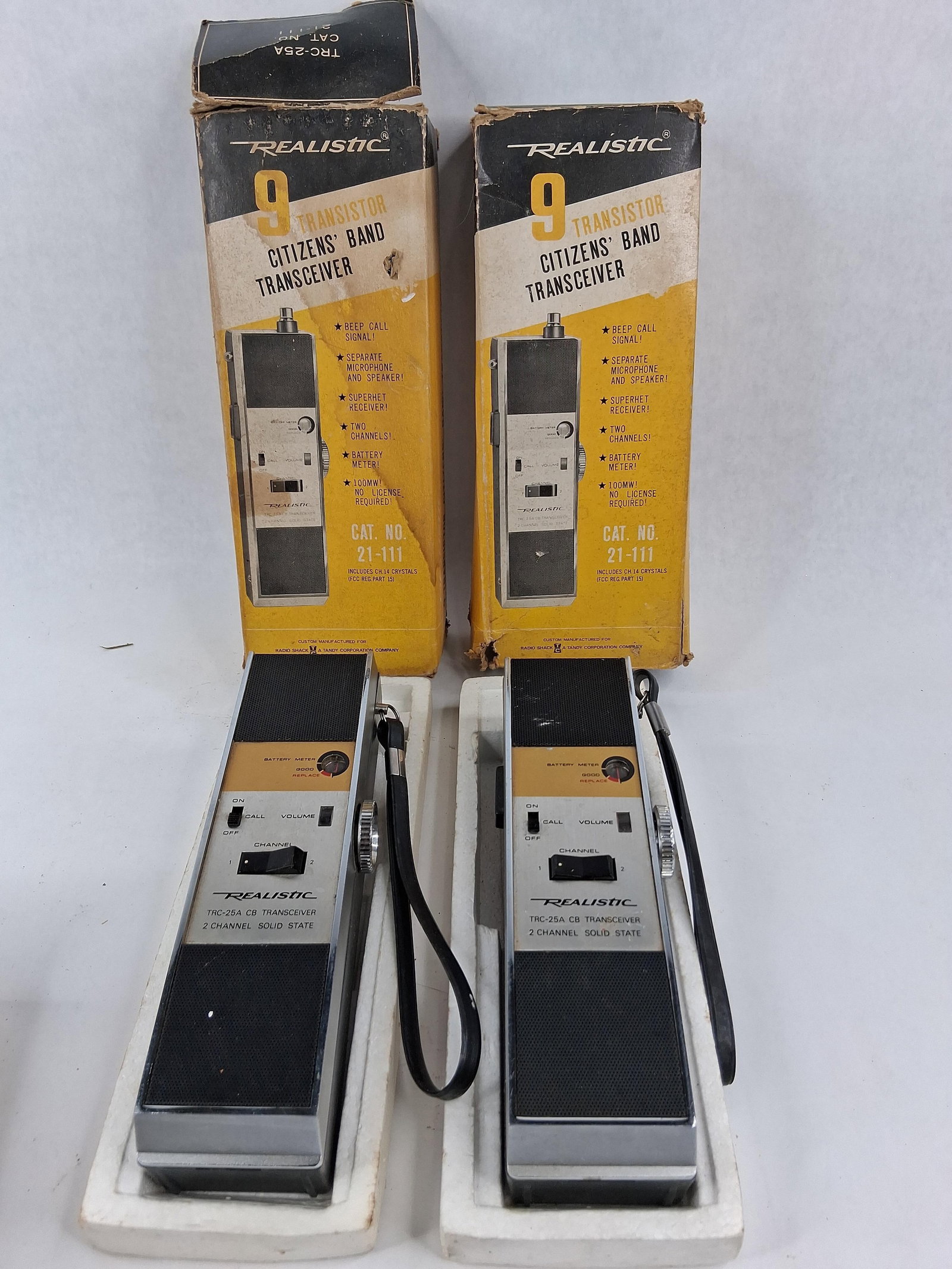 Realistic TRC-25A Transceivers w/ Boxes: This set comprises a pair of Realistic TRC-25A Citizens Band (CB) handheld transceivers, manufactured for Radio Shack, a Tandy Corporation company. Identified by catalog number 21-111, these 9-transis