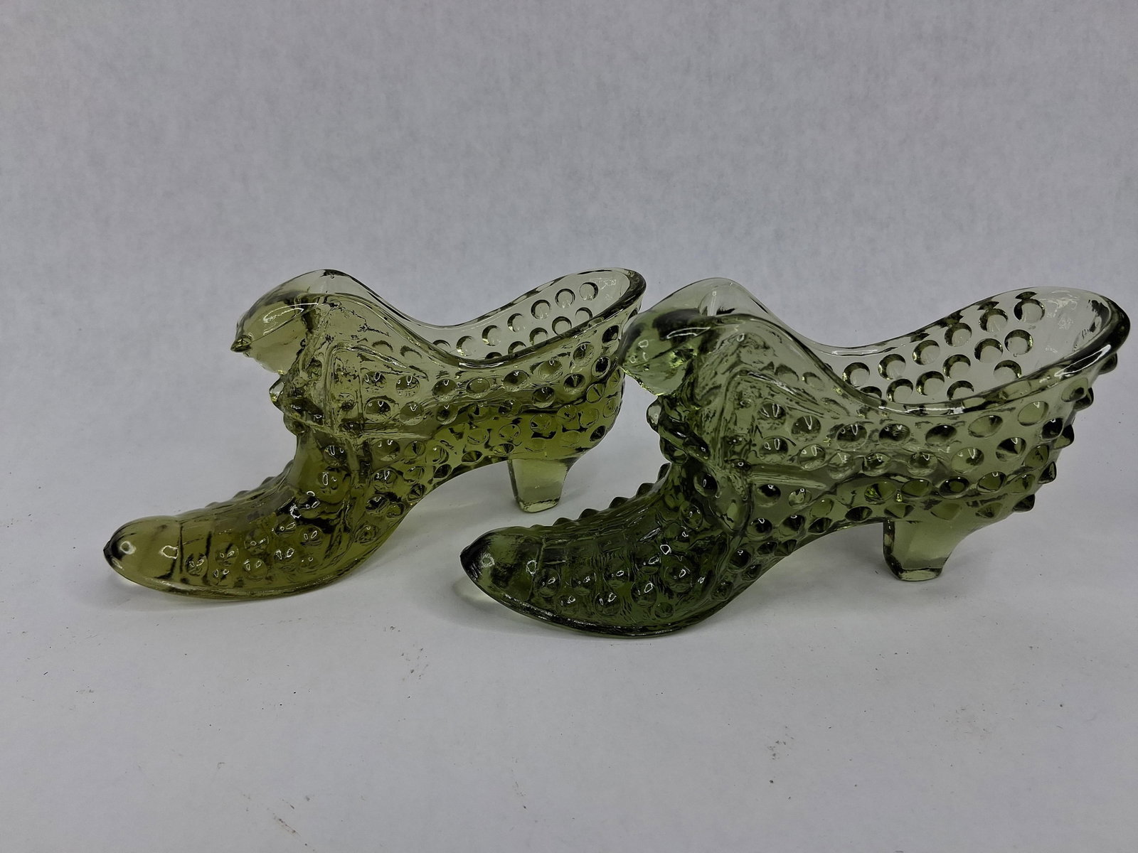 Fenton Green Hobnail Cat Head Glass: A pair of Fenton Art Glass Company decorative slippers in Colonial Green. Each piece is crafted from pressed glass in the form of a Victorian high-button boot featuring a tapered heel and pointed