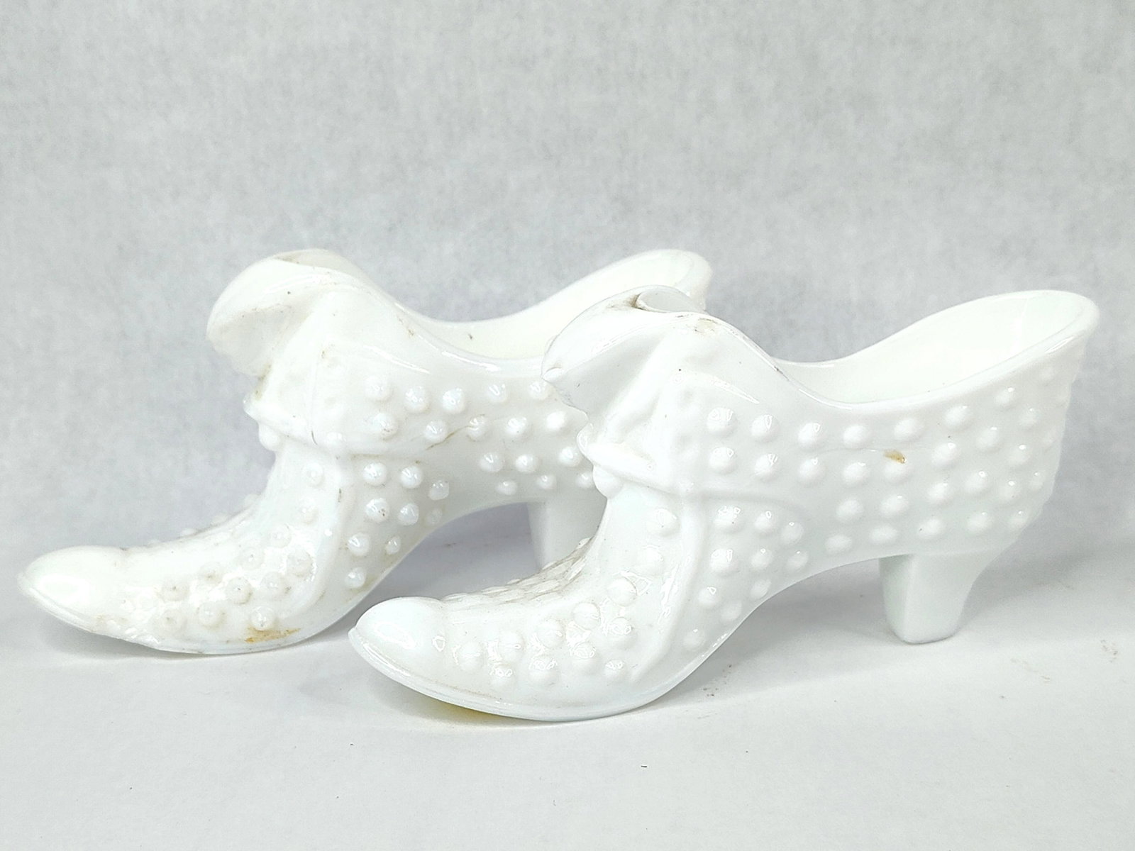 Pair Fenton Hobnail Cat Head Slippers: A matching pair of Fenton Art Glass Company miniature slippers crafted in opaque white milk glass. Each slipper features a hobnail pattern and is designed in a high-heel form with a molded cat head