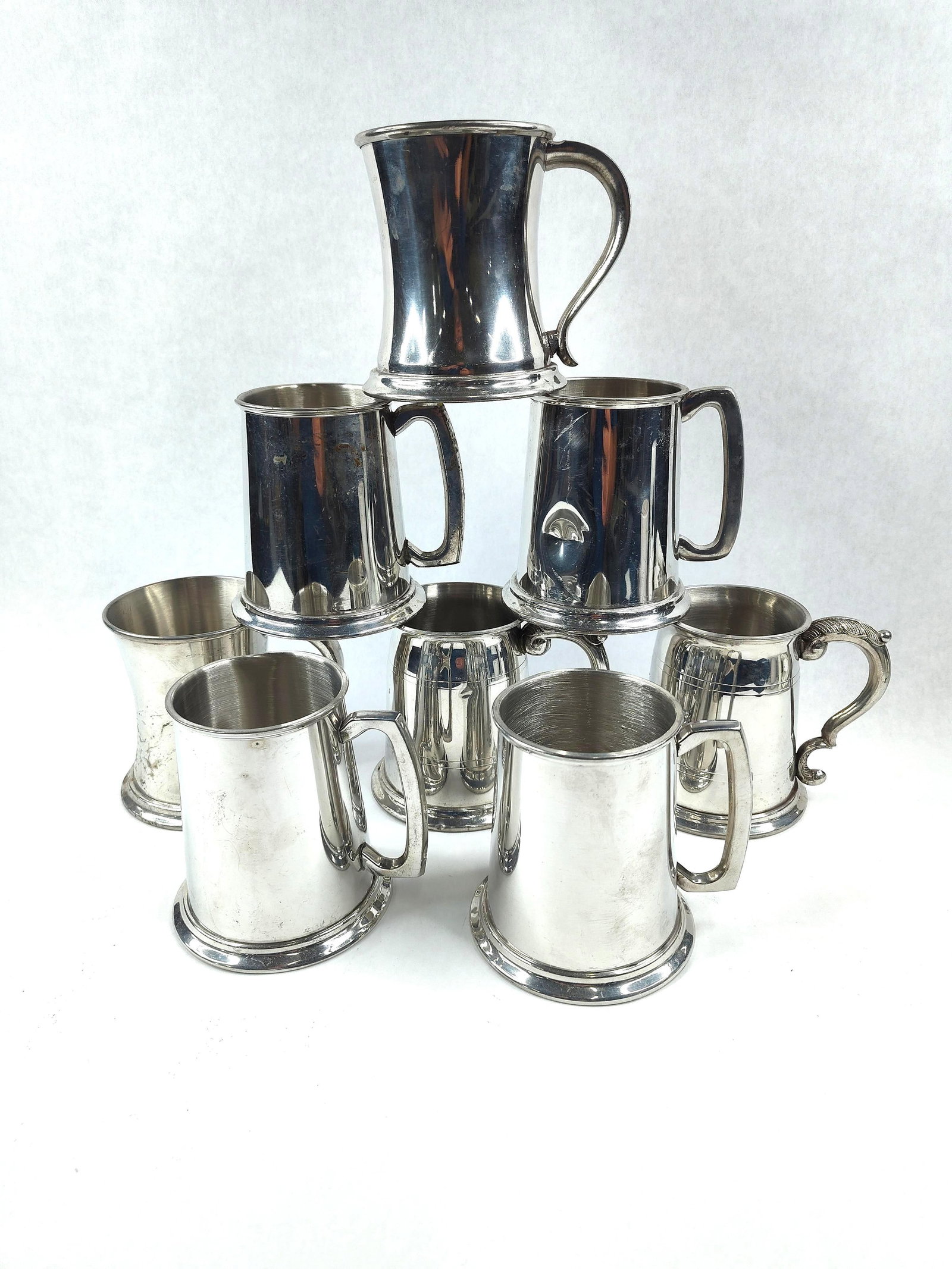 8 Sheffield Pewter Mugs & Tankards: This lot consists of eight pewter drinking vessels in various traditional English styles, manufactured in Sheffield, England. The collection includes four straight-sided cylindrical mugs with angular