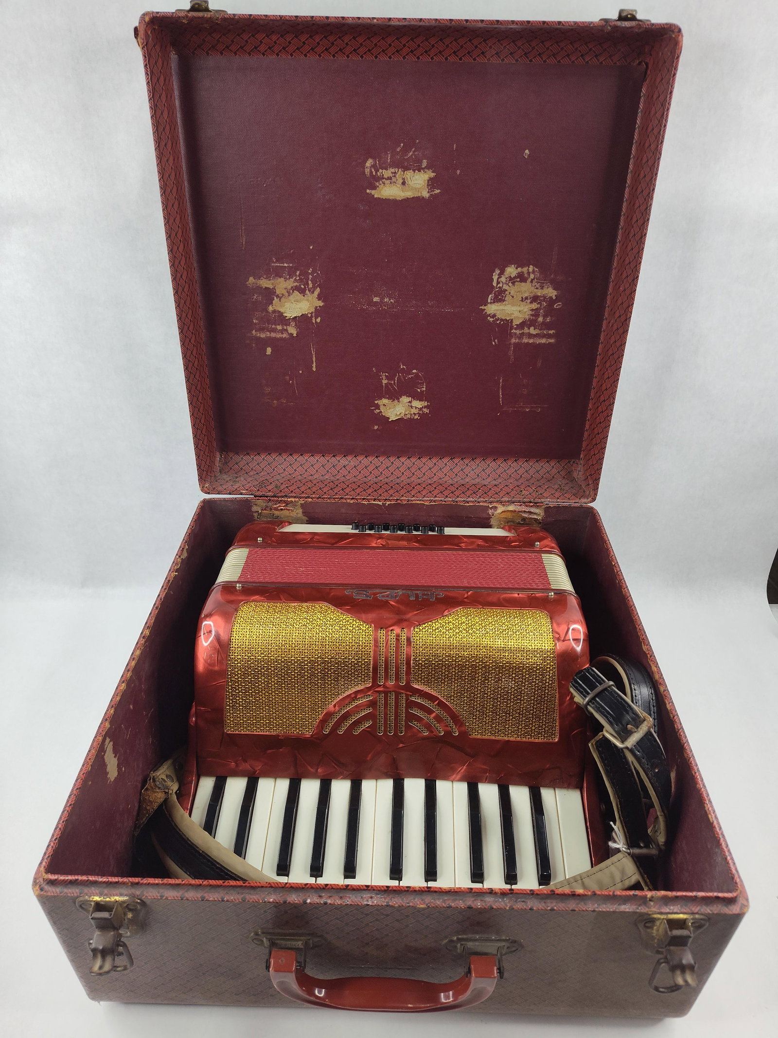 Hup's 12-Bass Piano Accordion w/ Case: This student piano accordion is manufactured by Hup's in Italy. It features a 25-key treble keyboard and a 12-button bass section arranged in two rows. The exterior is finished in a vibrant red