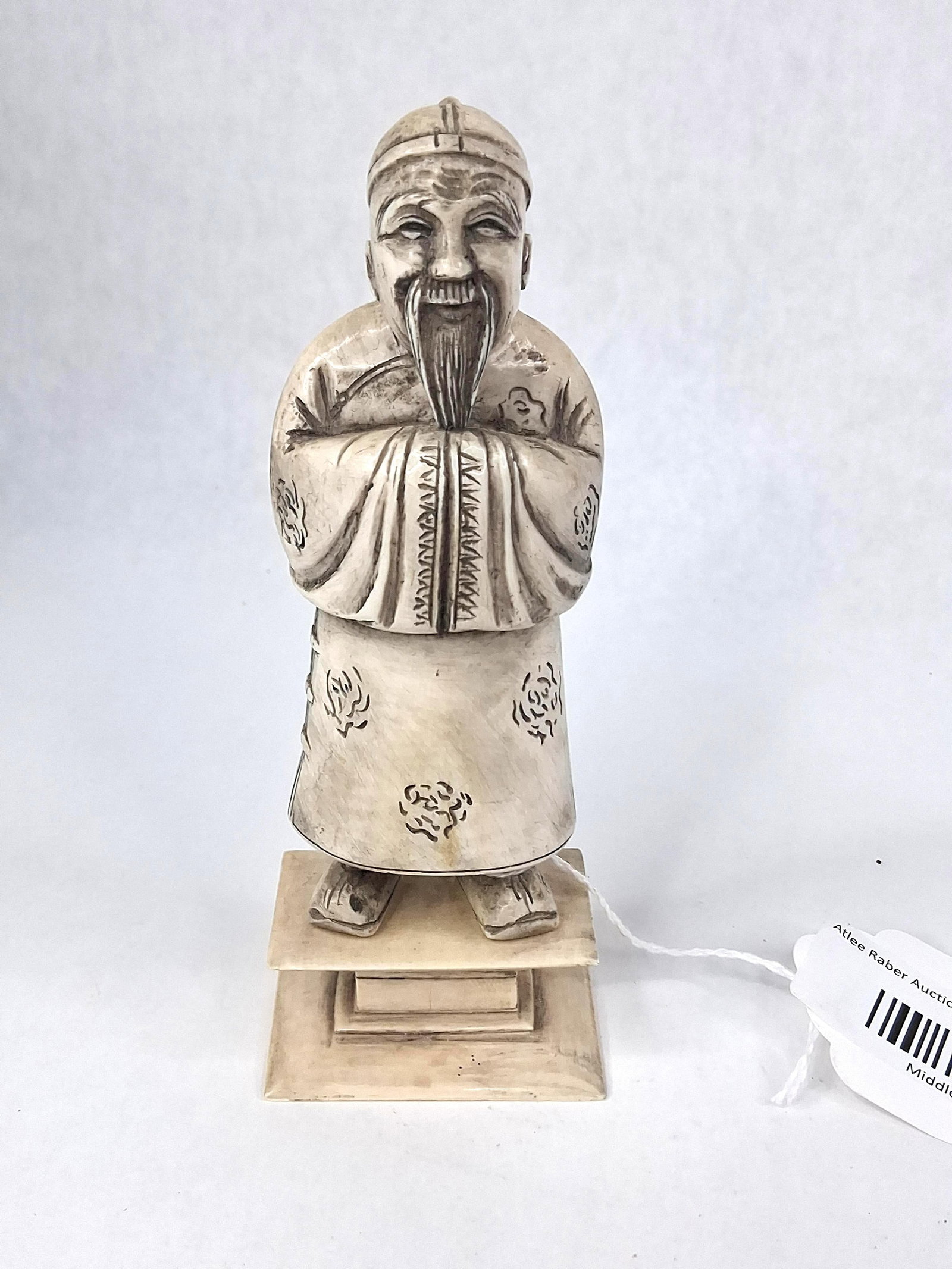 Chinese Ivory Qing Dynasty Elder Figure: This figure is a carved elephant ivory depiction of a standing Chinese elder or official, dated to the late 19th or early 20th century. The man is carved with a cheerful facial expression, a long