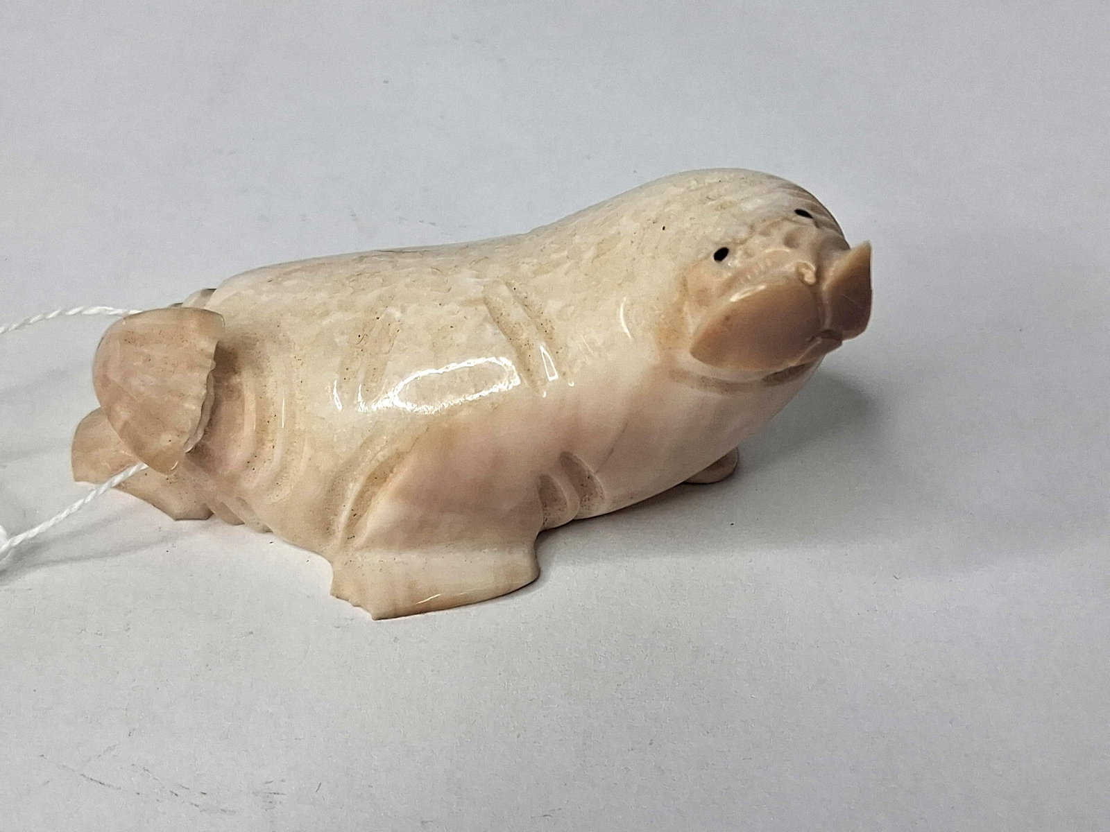 A.H.S. Inuit Ivory/Bone Walrus Figurine: This is a hand-carved animal figurine depicting a walrus, likely of Inuit origin. The object is fashioned from natural material featuring a creamy color and a polished surface. The underside of the