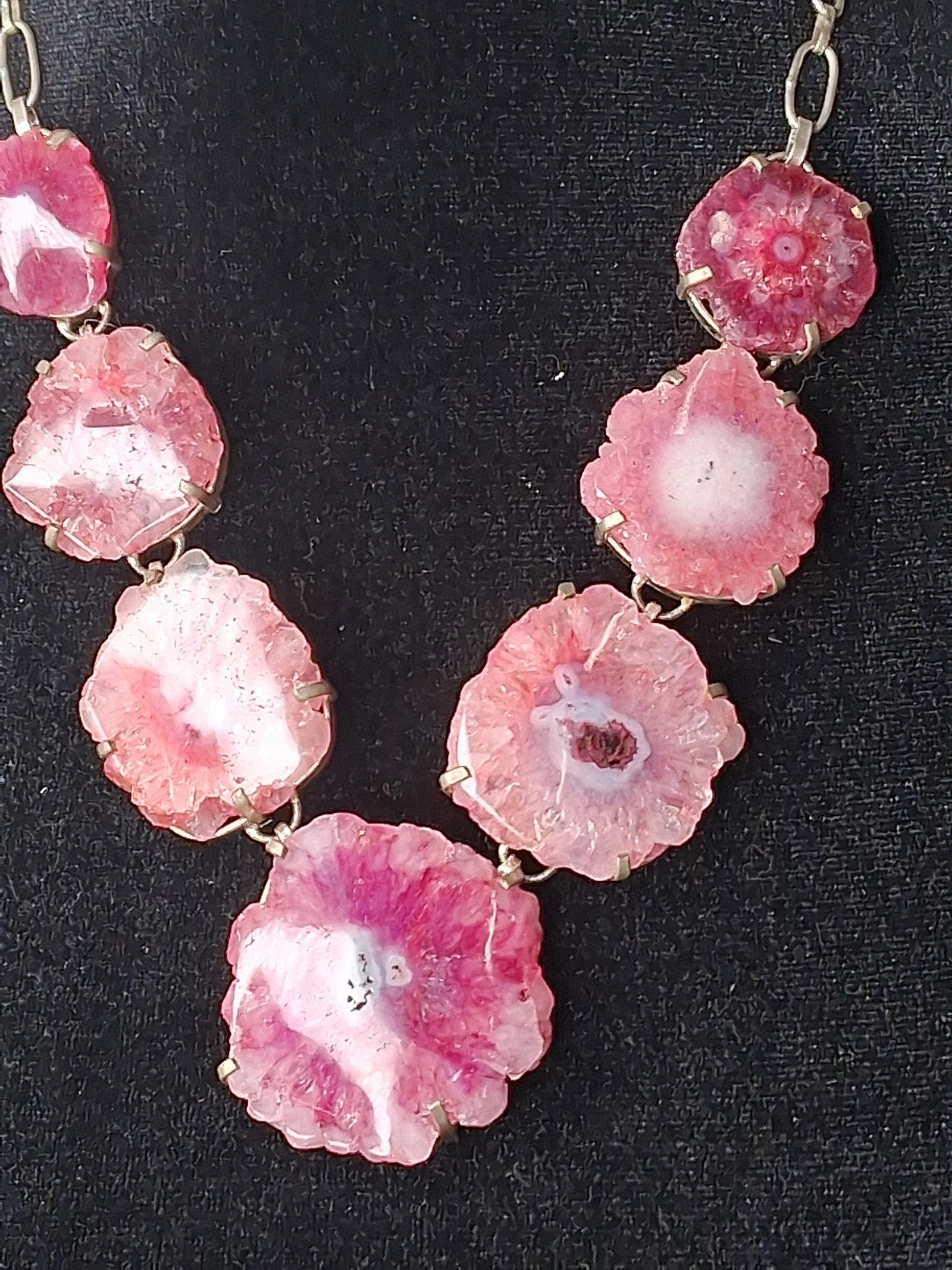 Pink Solar Quartz & Gold Tone Necklace: This statement collar necklace features seven graduated slices of dyed pink solar quartz, also known as sunflower agate. The organic gemstone slices exhibit a radial crystalline structure surrounding
