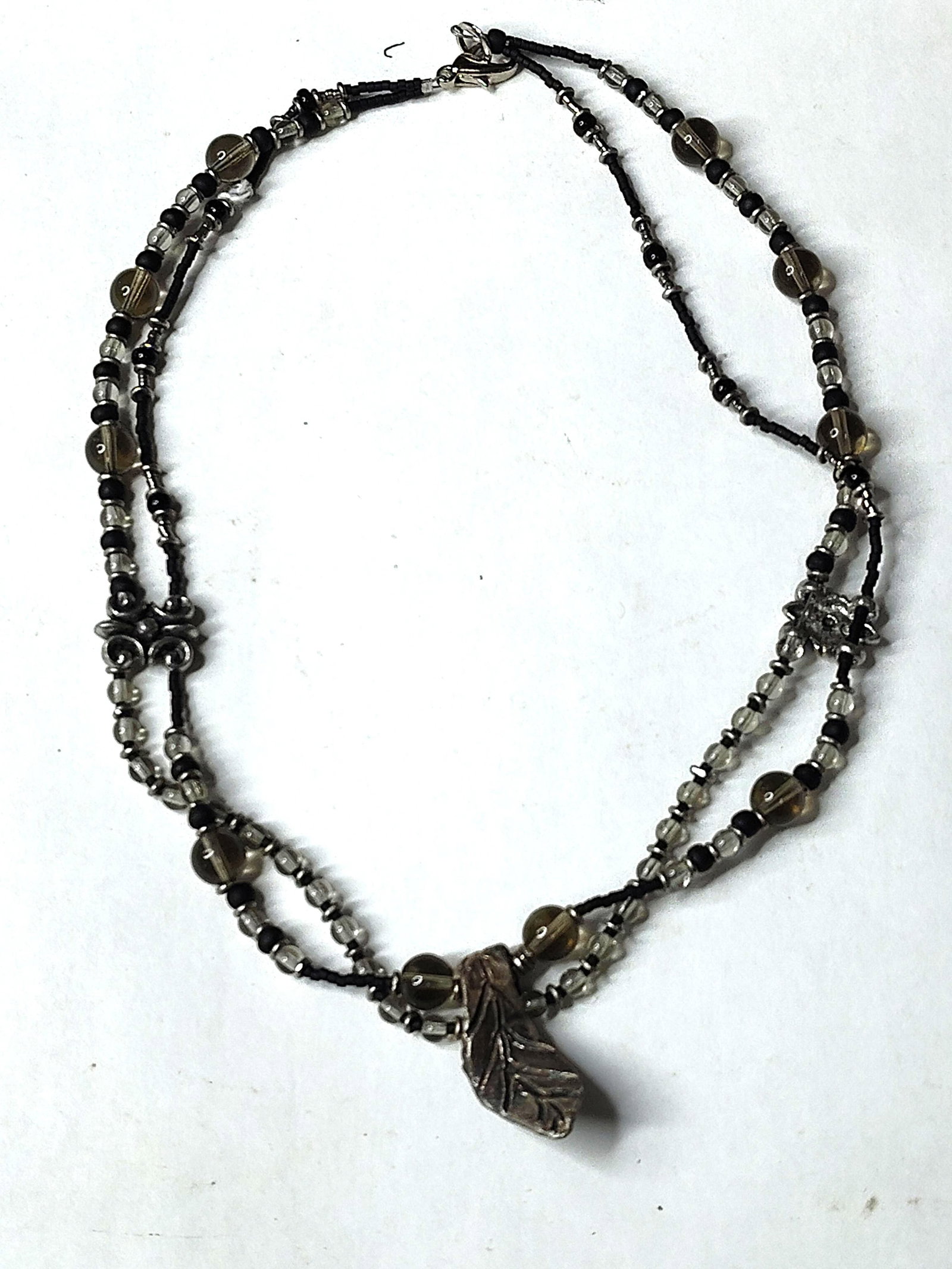 JJ Double Strand Beaded Leaf Necklace: A double-strand beaded necklace by the Jonette Jewelry Co. featuring a large nature-inspired leaf pendant. The necklace is constructed with two tiers of beads, including round translucent smoky-brown 