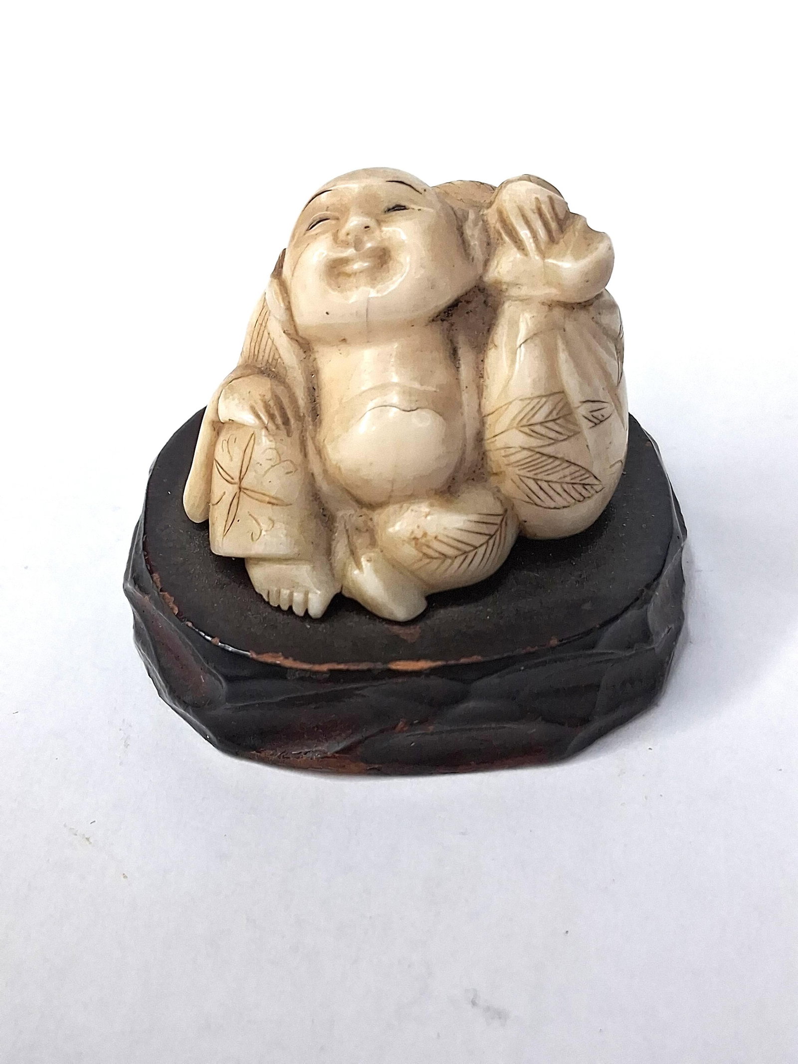 Japanese Ivory Hotei Okimono, Meiji: A hand-carved Japanese ivory okimono depicting Hotei, one of the Seven Lucky Gods. The figure is rendered in a seated position with a laughing expression and a large belly, holding a traditional cloth