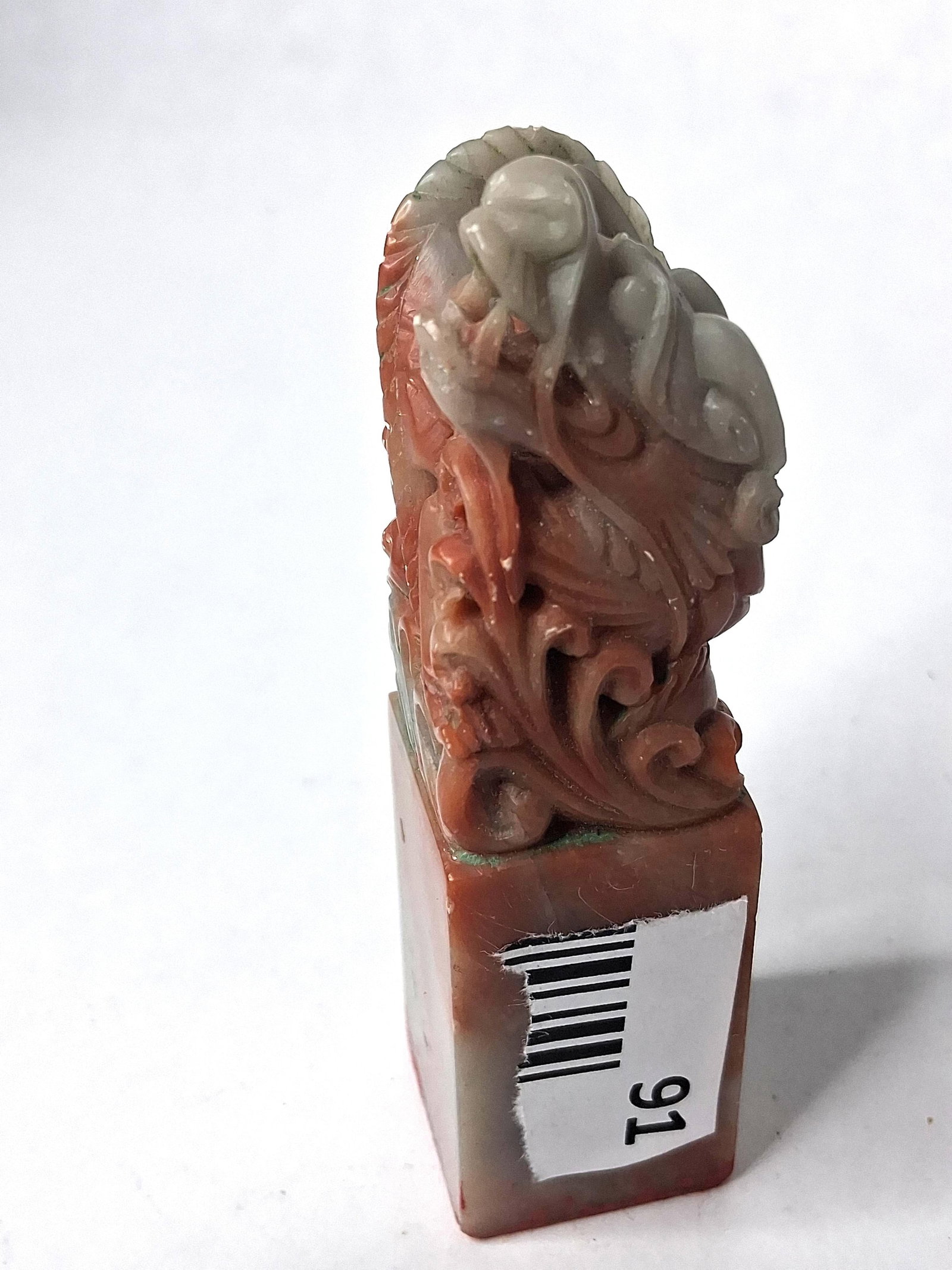 Chinese Shoushan Stone Mythical Seal: A carved Chinese Shoushan stone seal featuring natural tri-color mottling in shades of russet red, gray-green, and pale cream. The stone exhibits a characteristic waxy luster. The seal is topped with