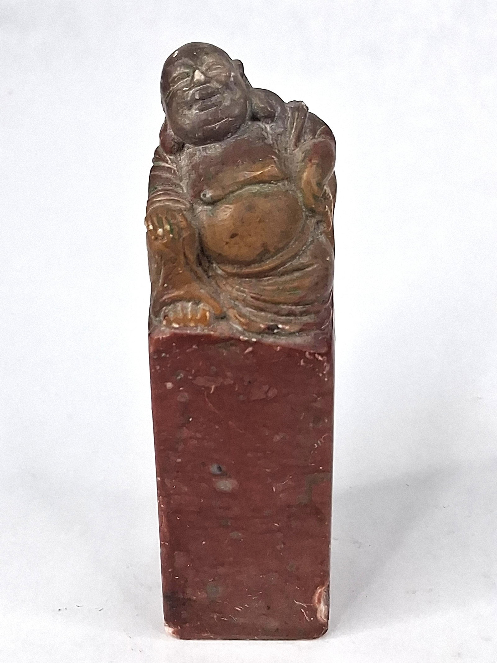 Chinese Soapstone Seal w/ Budai Finial: A Chinese carved stone seal featuring a rectangular pedestal base topped with a hand-carved finial of Budai, the Laughing Buddha. The figure is depicted in a seated pose with a prominent belly and a s
