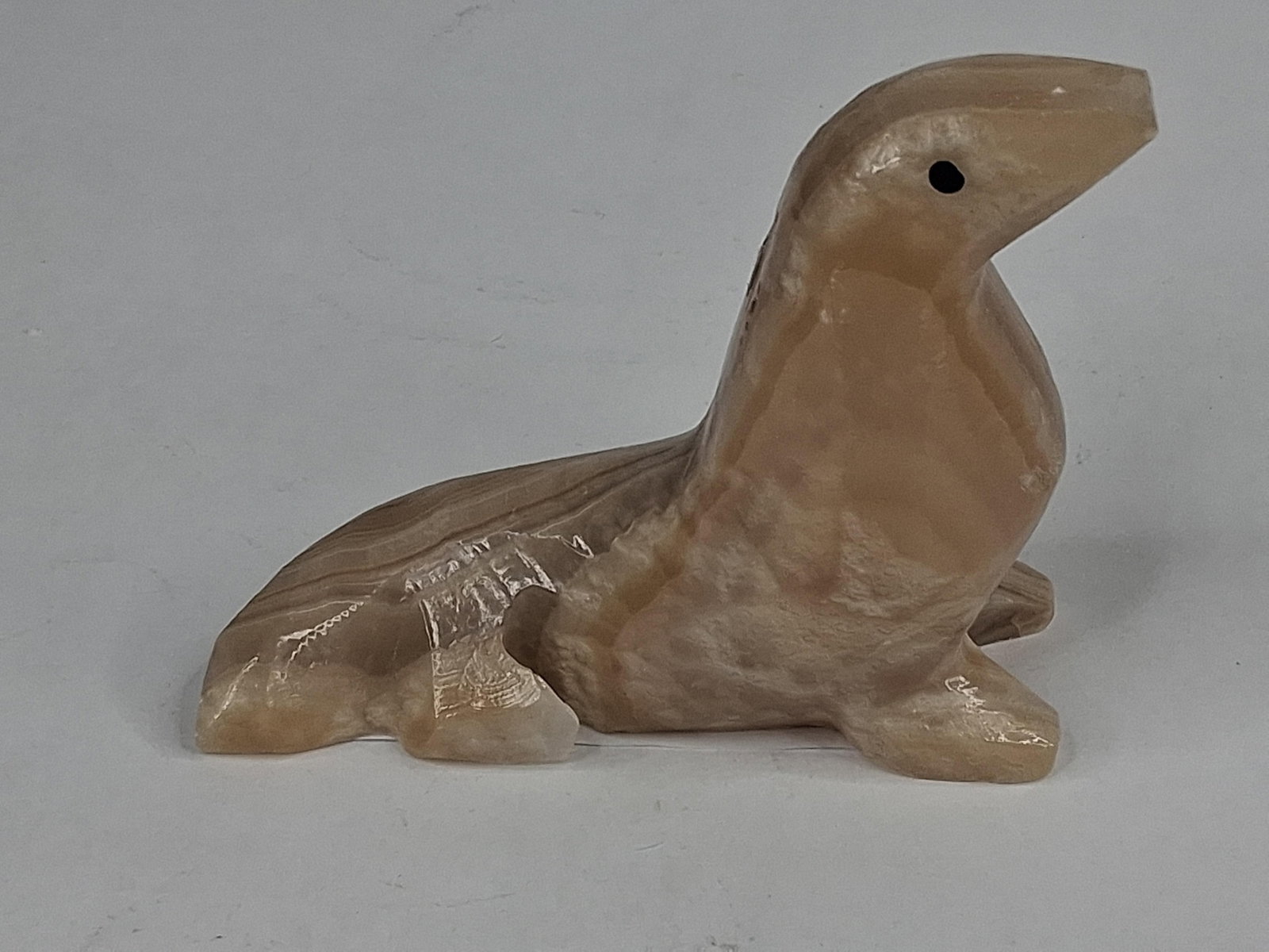 Carved Banded Onyx Seal Figurine: This figurine depicts a seal or sea lion in an upright, alert posture, hand-carved from banded onyx, a variety of calcite. The piece displays characteristic horizontal layering in alternating bands of