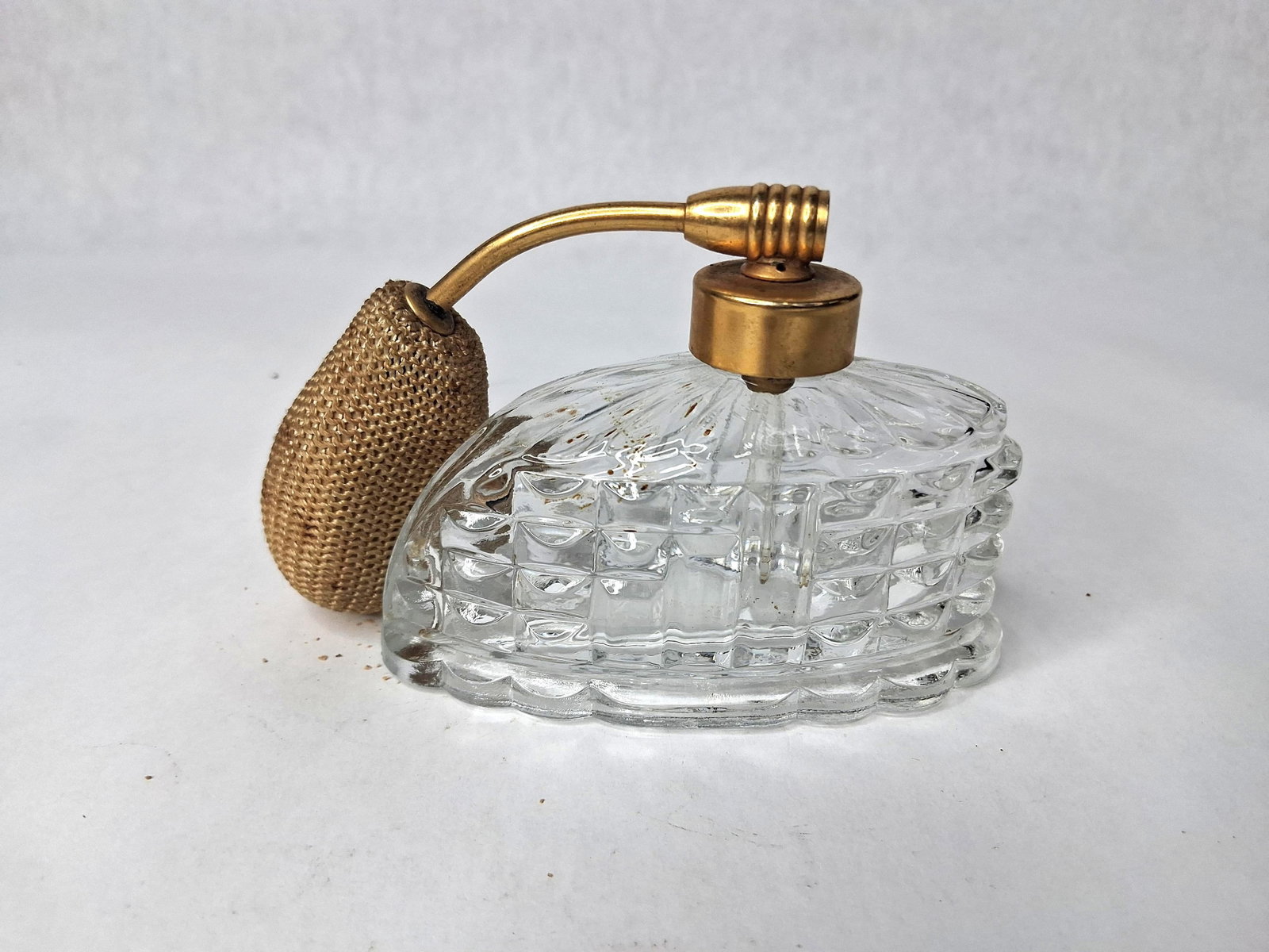 Holmspray Mid-C. Pressed Glass Atomizer: A mid-century perfume atomizer bottle by Holmspray featuring a clear pressed glass vessel in an elongated boat shape. The glass is decorated with a relief-molded quilted pattern on the lower portion a