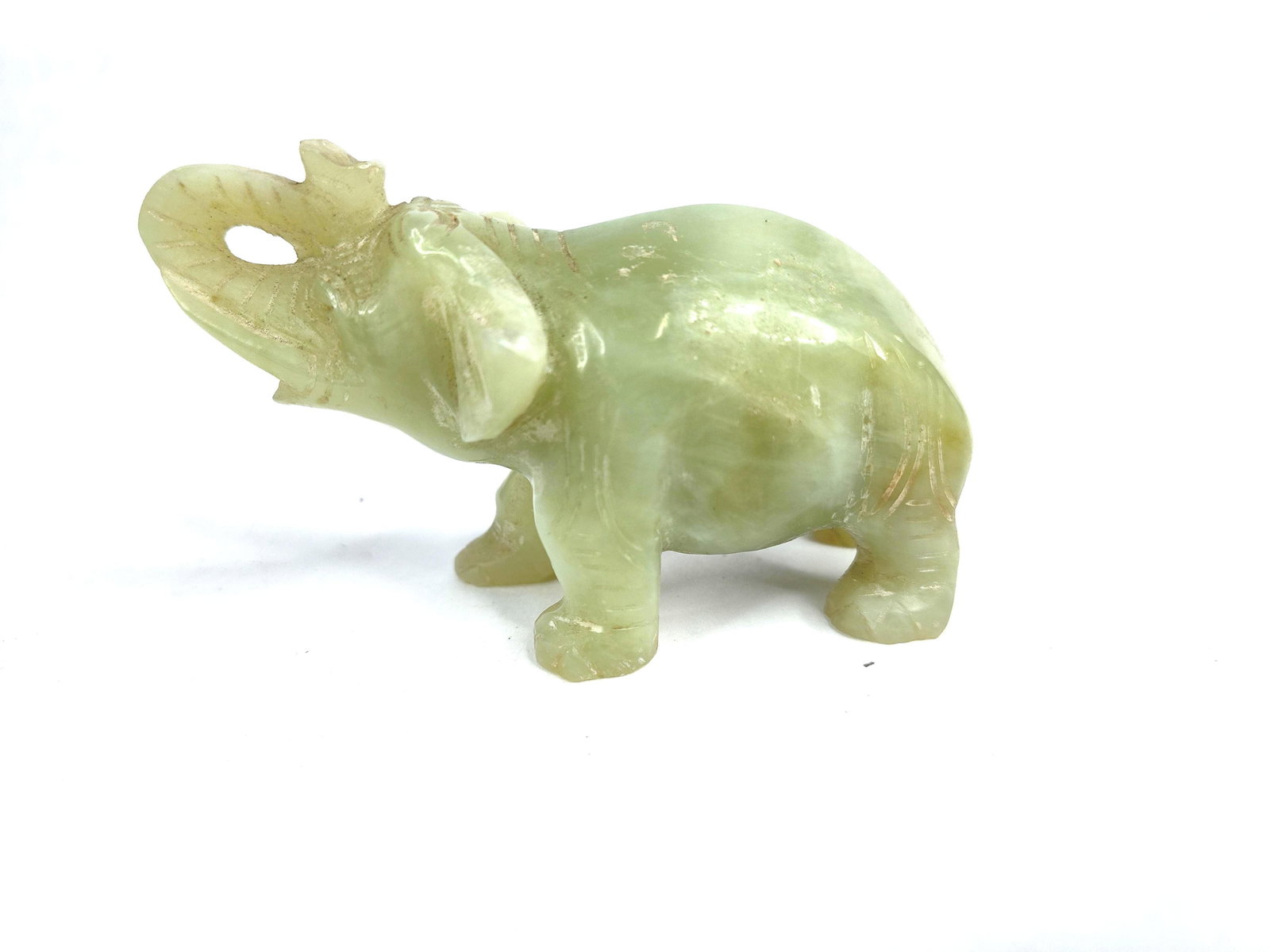 Carved Light Green Hardstone Elephant: A hand-carved hardstone figurine depicting a standing elephant with its trunk raised. The object is fashioned from a light green, semi-translucent stone, consistent with jade or serpentine, featuring 