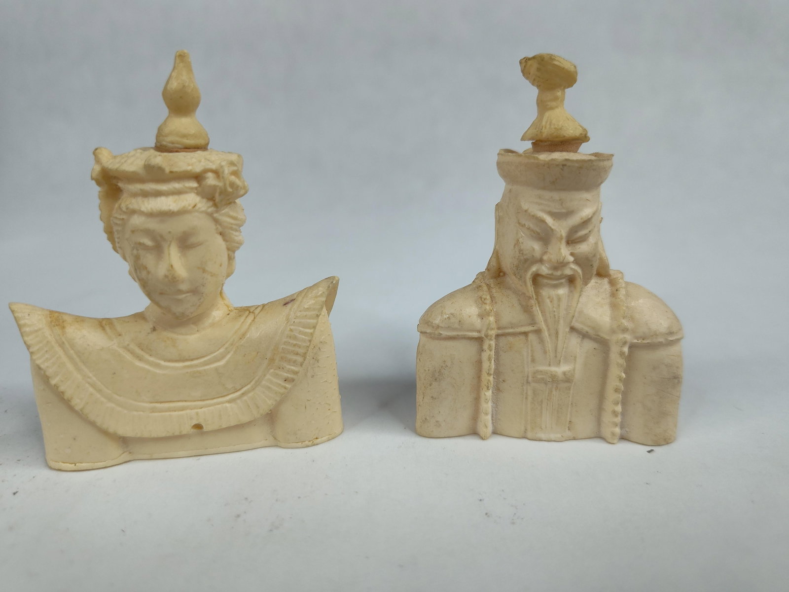 Pair Chinese Emperor/Empress Figurines: A pair of miniature decorative busts crafted from cream-colored molded resin designed to simulate carved ivory. The figurines depict a Chinese Emperor and Empress in traditional ceremonial attire. The