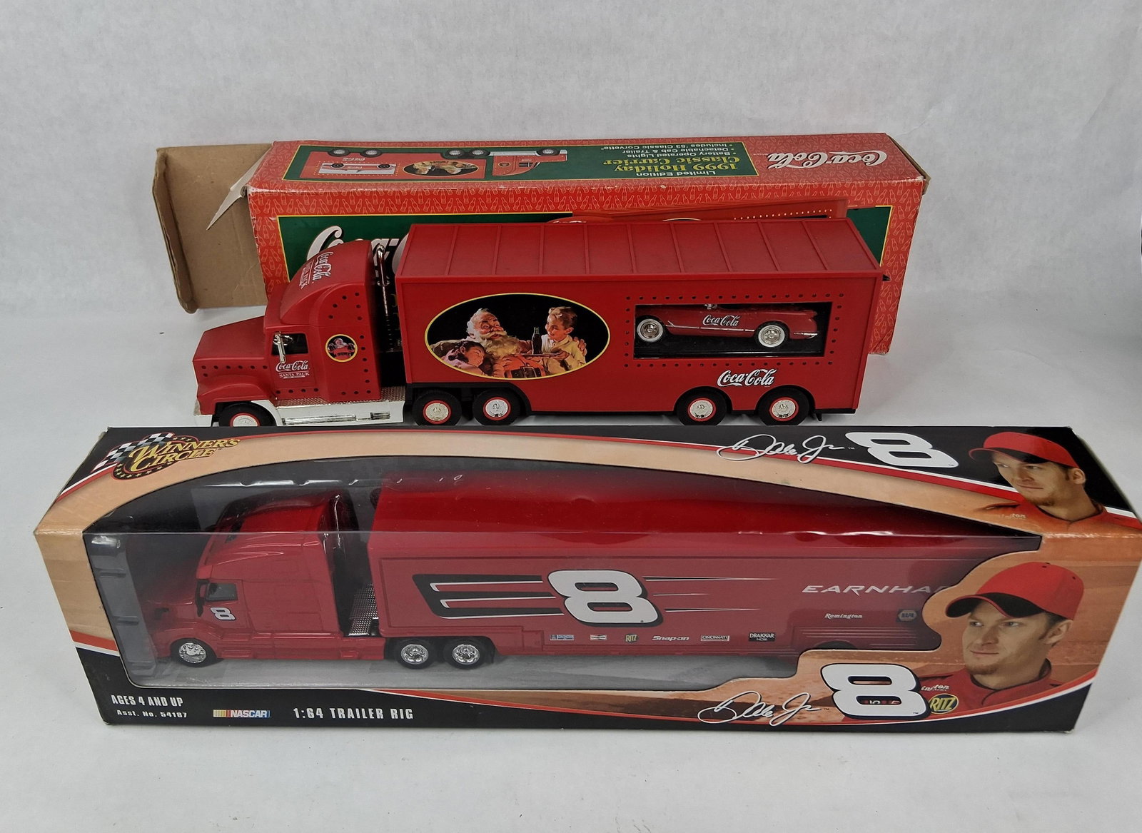 Pair Boxed Coca-Cola & NASCAR Trucks: This lot comprises two boxed collectible toy tractor-trailer rigs. The first item is a Coca-Cola 1999 Holiday Classic Carrier, a limited edition battery-operated toy. It is constructed from red plasti