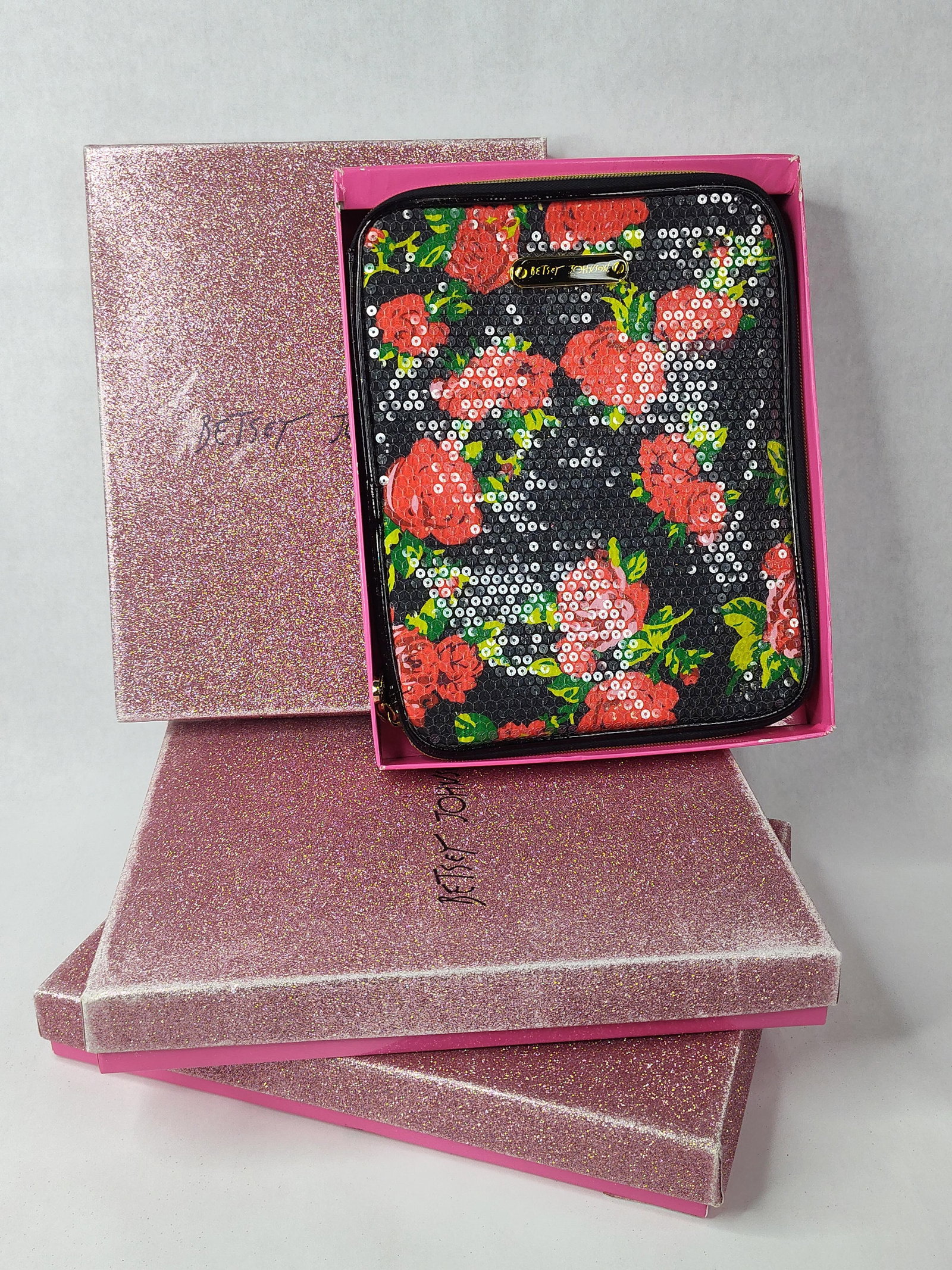 Betsey Johnson Tablet Cases Collection: A group of Betsey Johnson designer tablet cases. This lot features two distinct styles of zip-around sleeves: a floral pattern on a black ground with a clear sequin overlay and a solid gold glitter