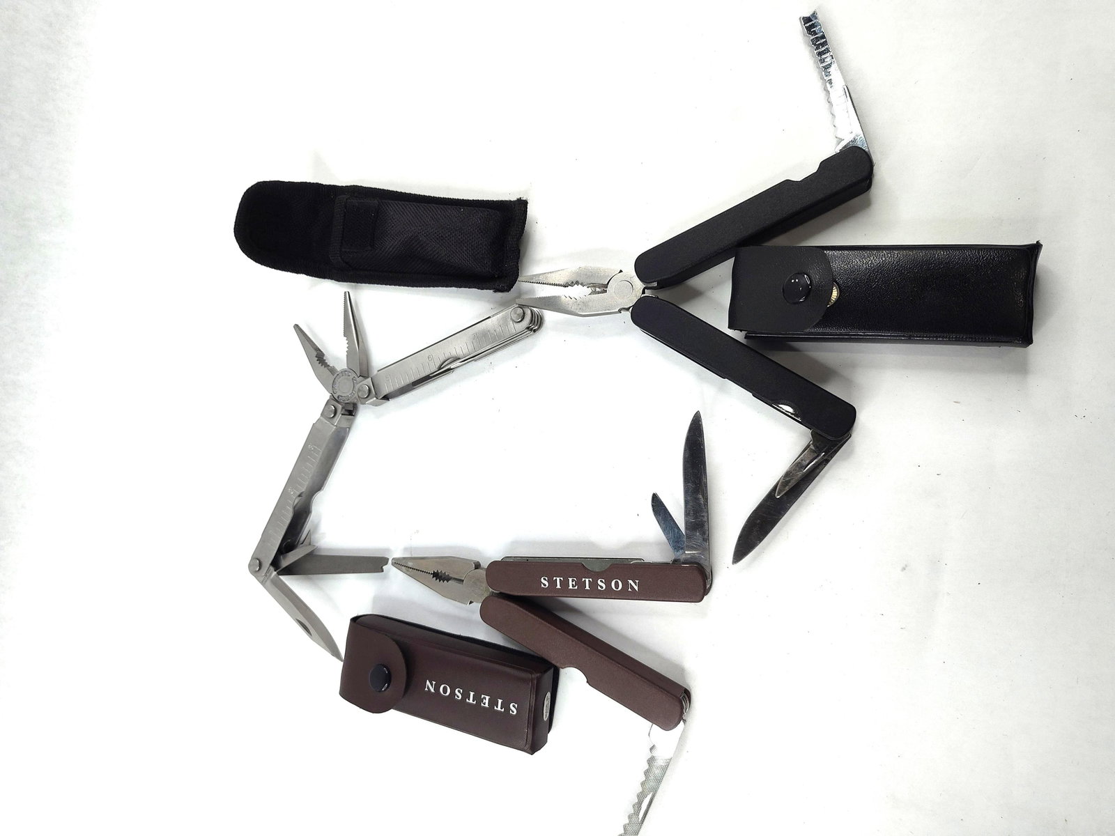 Garrity & Stetson Folding Multi-Tools: A trio of assorted folding multi-tools, each provided with a protective carrying sheath. The first item is a stainless steel multi-tool featuring needle-nose pliers, wire cutters, a plain edge knife b