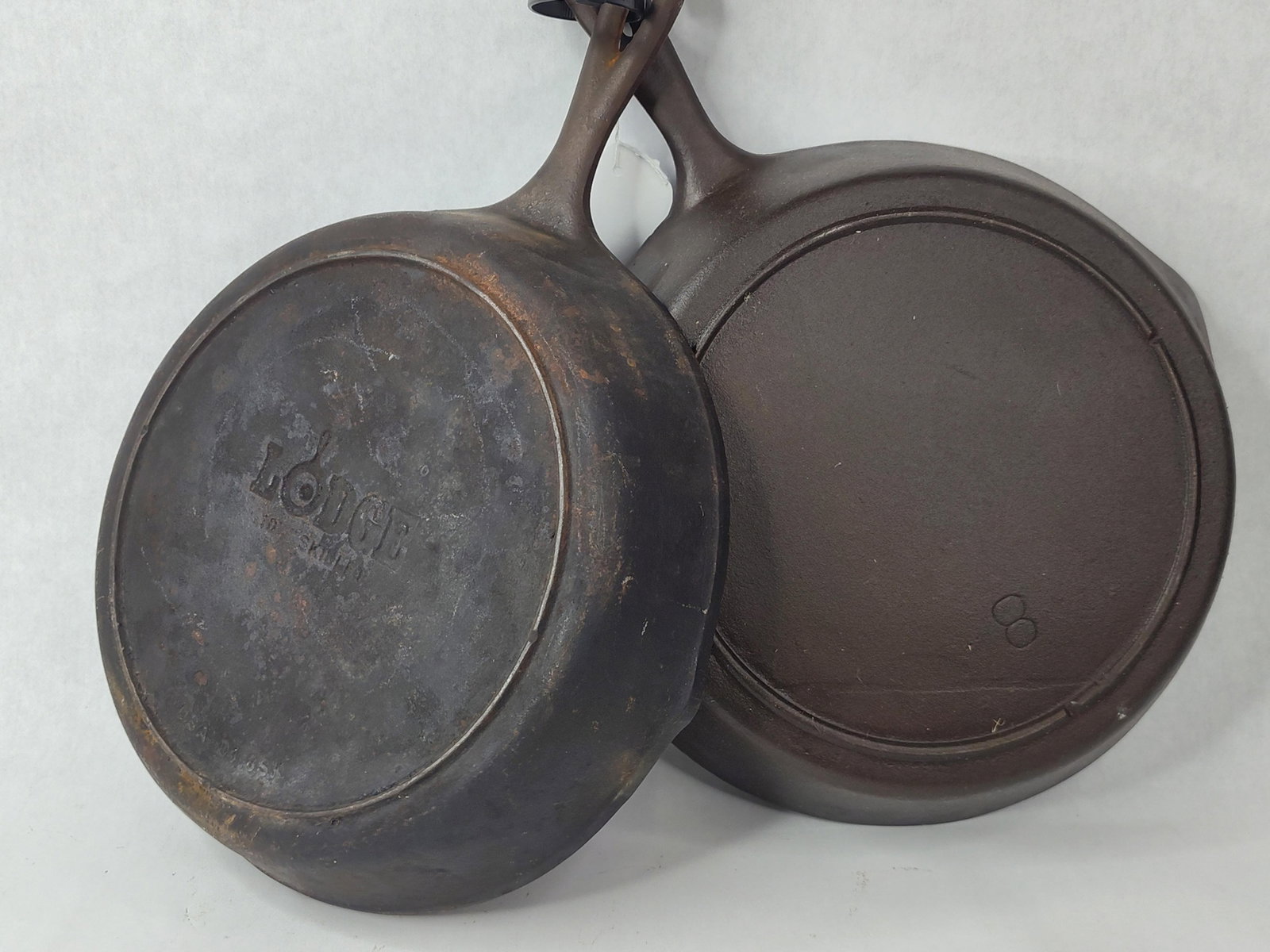 Pair Lodge Cast Iron Skillets: Two cast iron skillets manufactured by the Lodge Manufacturing Company of South Pittsburg, Tennessee. The collection includes a size number 10 skillet and a size number 8 skillet. The size 10 skillet 