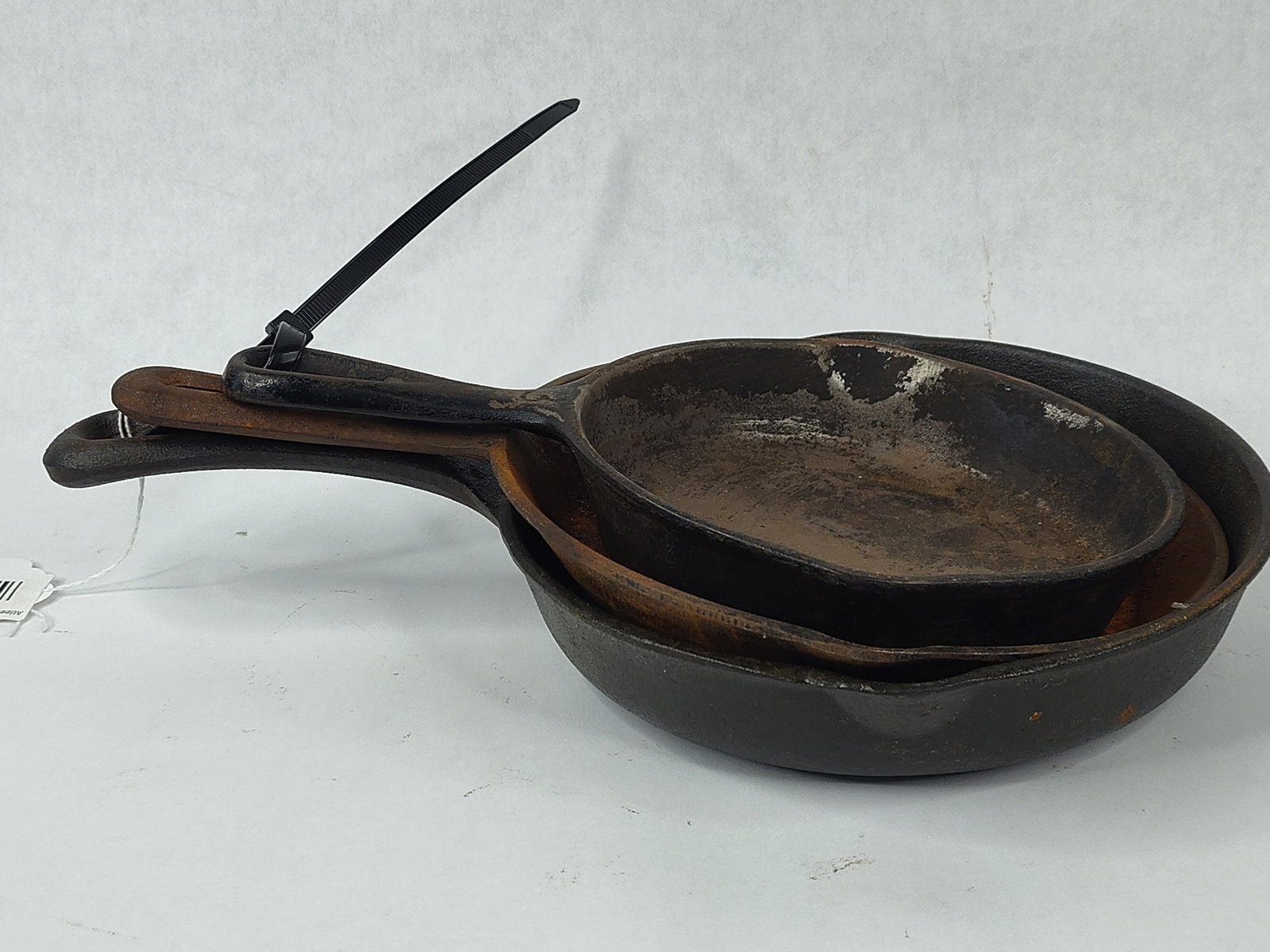 A Trio of Cast Iron Skillets: This lot consists of a trio of nested cast iron skillets in graduated sizes. Each vessel features a traditional round form with dual integrated pouring spouts and a tapered handle with a circular