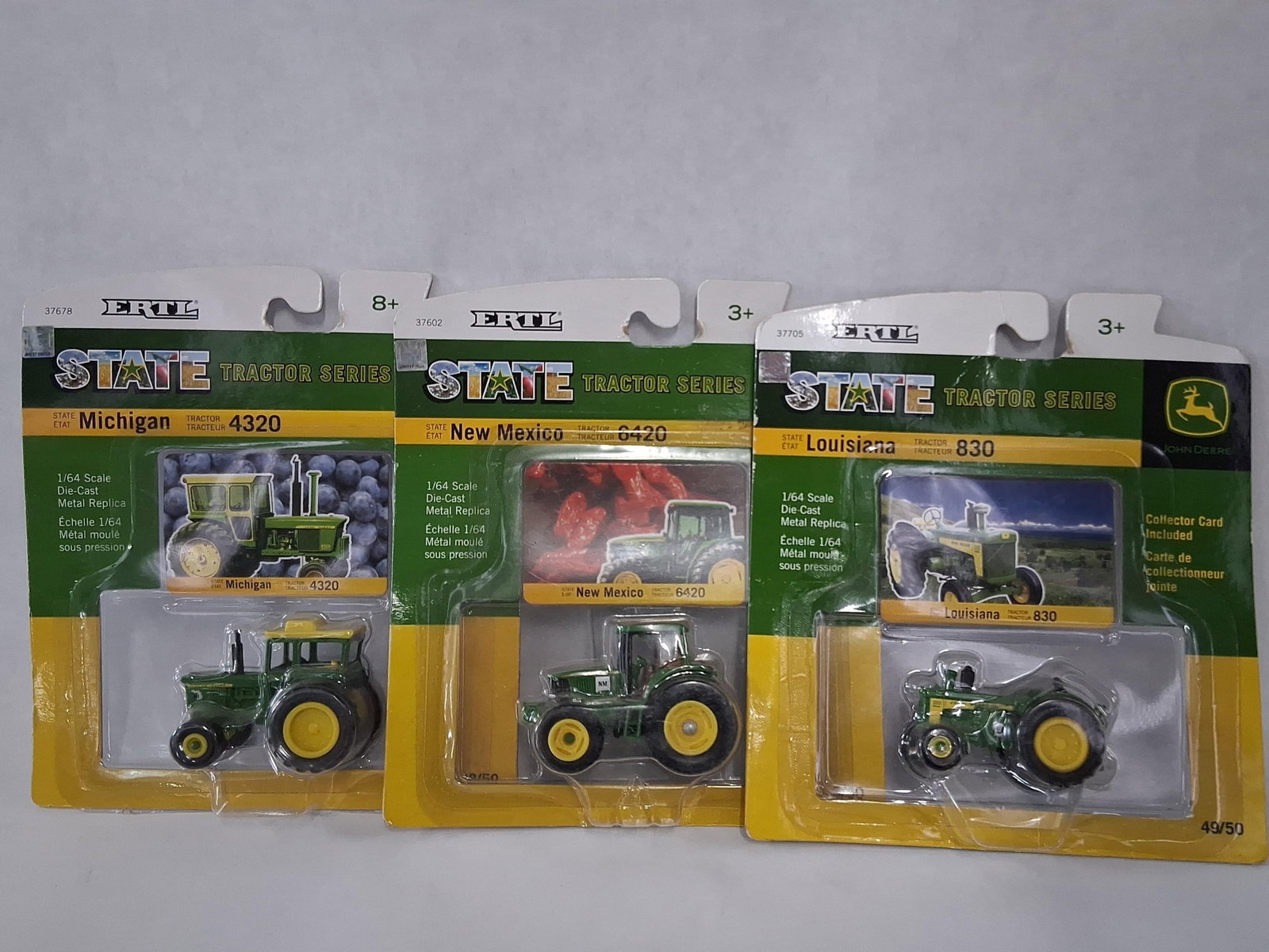 3 ERTL 1/64 John Deere State Tractors: A trio of John Deere toy tractors from the ERTL State Tractor Series, manufactured by Learning Curve Brands, Inc. These 1/64 scale replicas are constructed from die-cast metal with plastic components 
