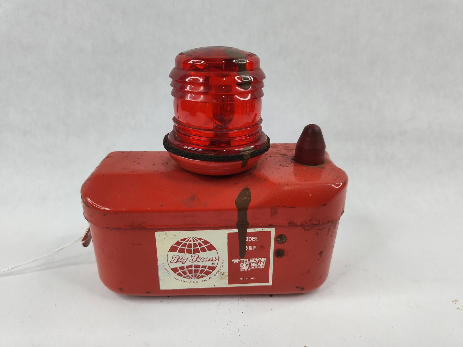 Teledyne Big Beam 108 F Hazard Lantern: This industrial emergency beacon is a Teledyne Big Beam Model 108 F hazard lantern. The unit features a red-painted steel housing with a hinged lid secured by a side latch. A red plastic