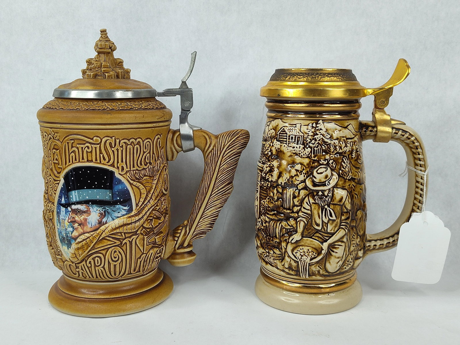 Pair Avon Steins: Christmas & Gold Rush: This lot contains two collectible lidded ceramic beer steins manufactured by Ceramarte in Brazil for Avon Products, Inc. The first stein, titled A Christmas Carol, is dated 1996. It features
