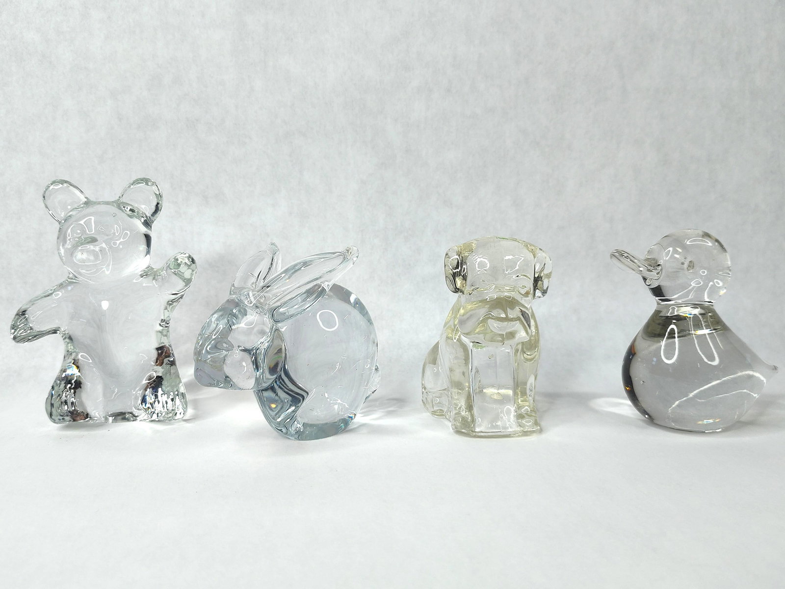 A Set of Clear Crystal Animal Figurines: A set of stylized animal figurines crafted from clear, colorless lead crystal. The collection features a standing bear depicted in a waving pose with one paw raised; a crouching rabbit with prominent 