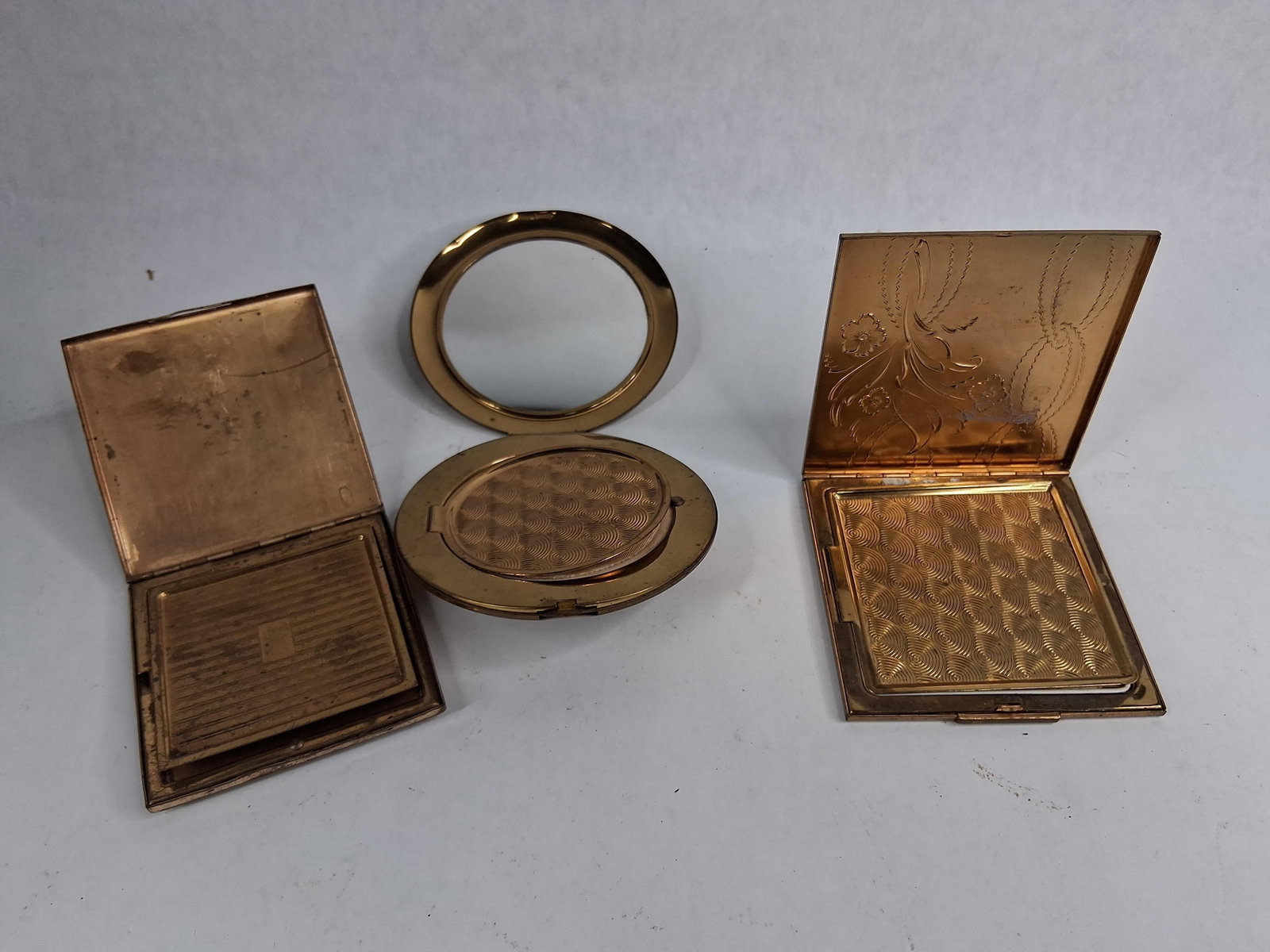 Trio Vtg Zell & Elgin American Compacts: A trio of mid-20th-century American vanity powder compacts manufactured by Zell Fifth Avenue and Elgin American. The collection consists of two square compacts and one circular compact, all