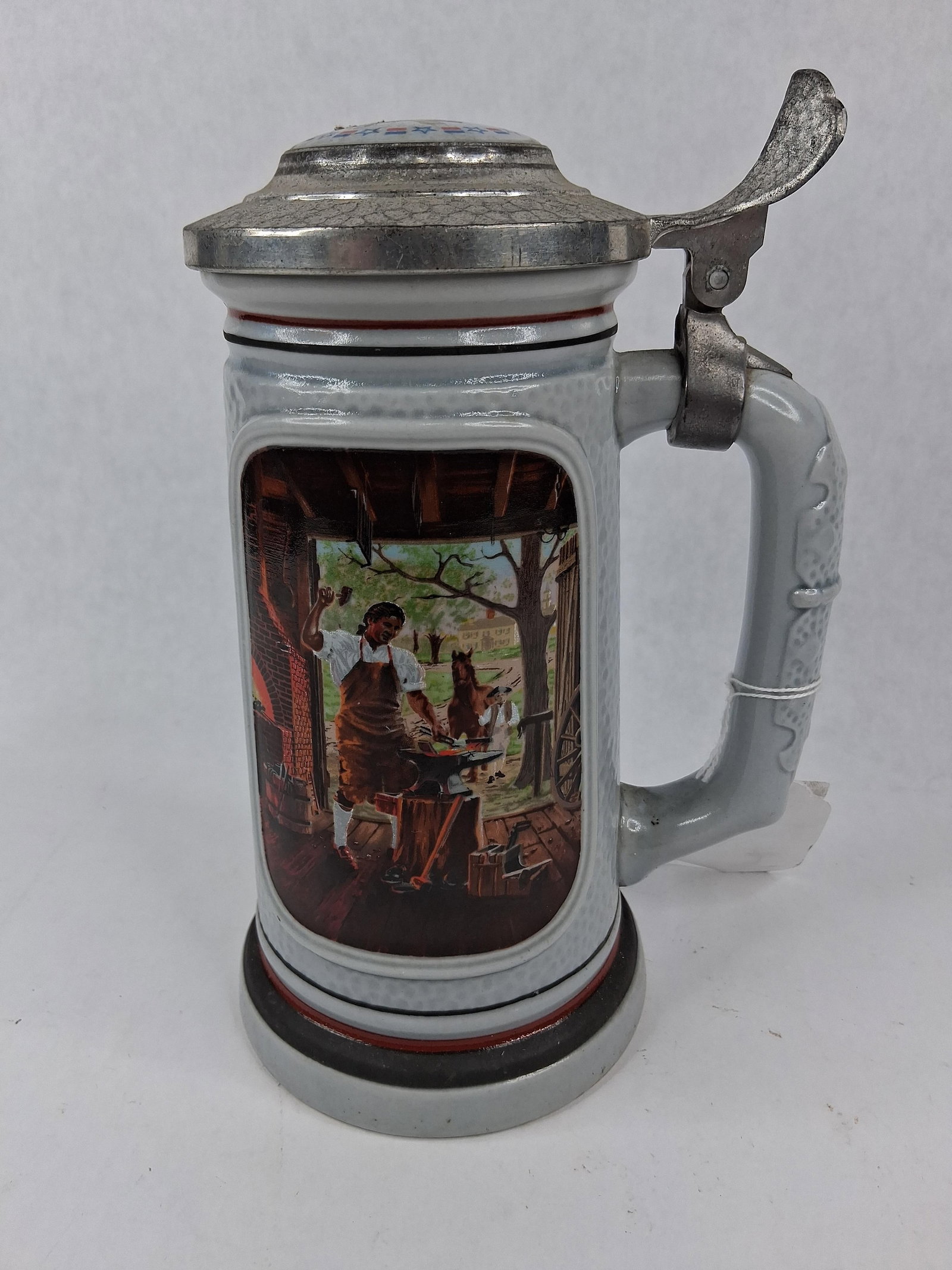 1985 Avon Blacksmith America Beer Stein: This is a glazed ceramic beer stein from the 1985 Avon Products Inc. series titled The Building of America Stein Collection. This specific piece is titled The Blacksmith and features artwork by artist